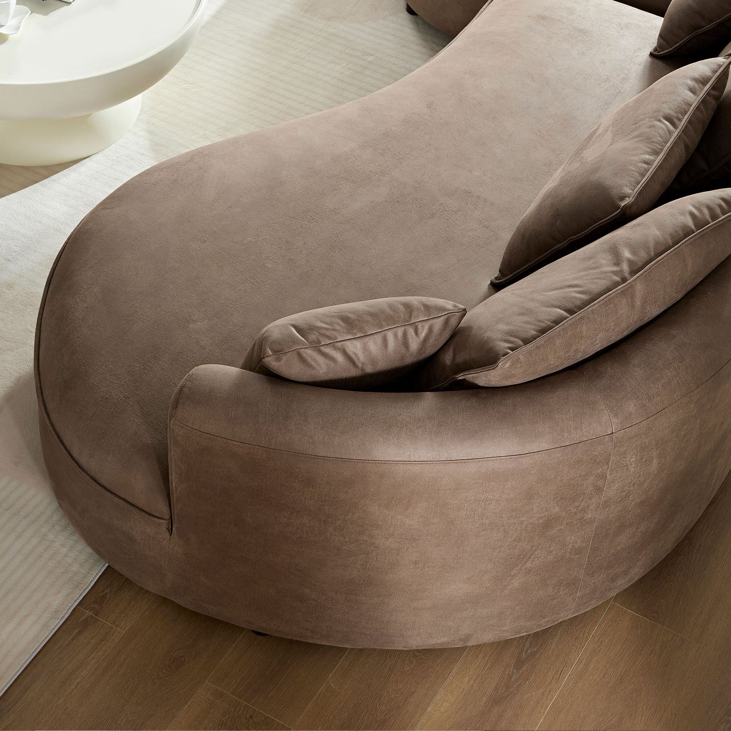 Curved taupe velvet sectional sofa with plush throw pillows and a matching ottoman