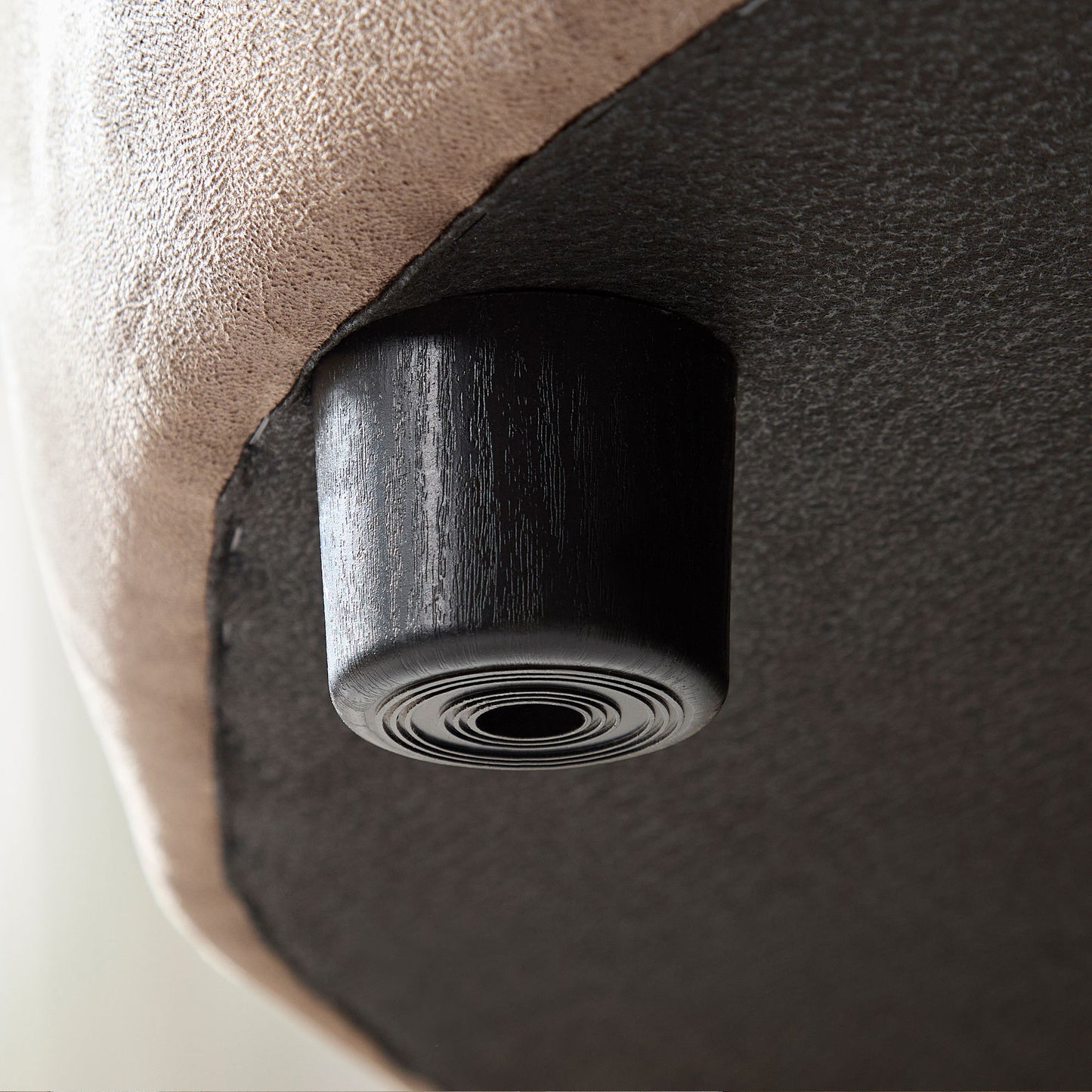 Closeup of a black textured furniture foot on a tan upholstered sofa