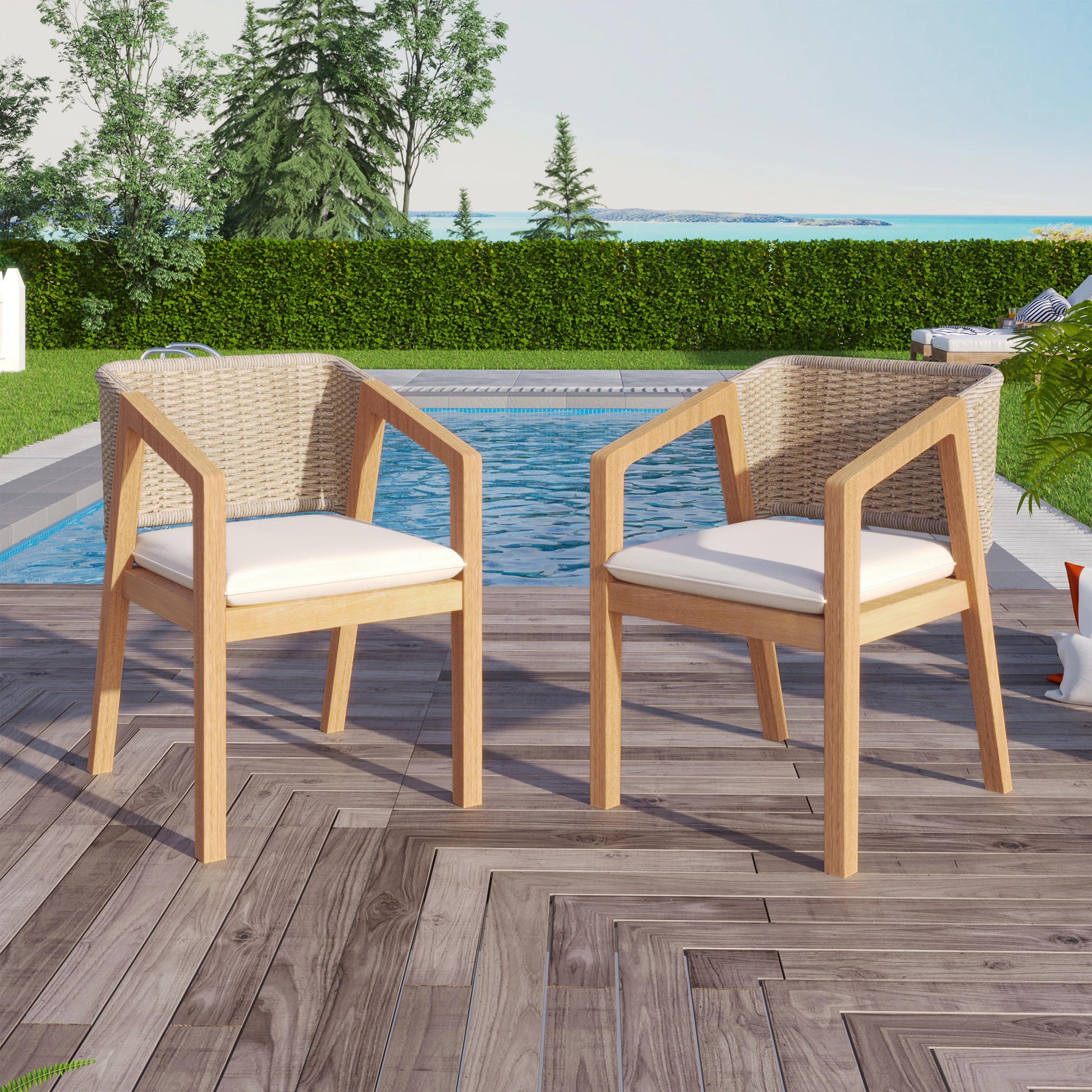 Two wicker outdoor chairs with white cushions on a wooden deck by a pool