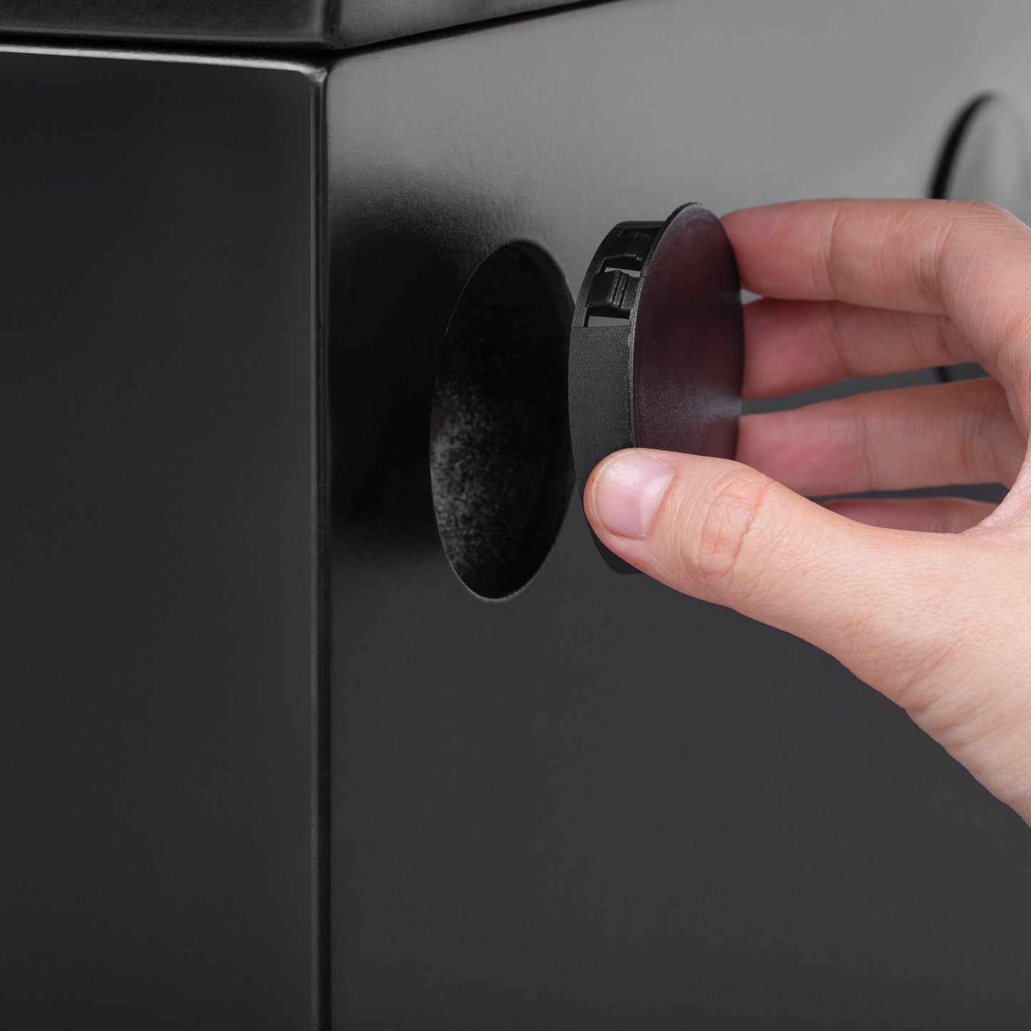 Closeup of a hand inserting a black round cap into a vent hole on a black metal appliance