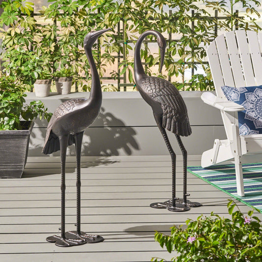 Pair of dark bronze metal heron statues standing gracefully on a wooden deck