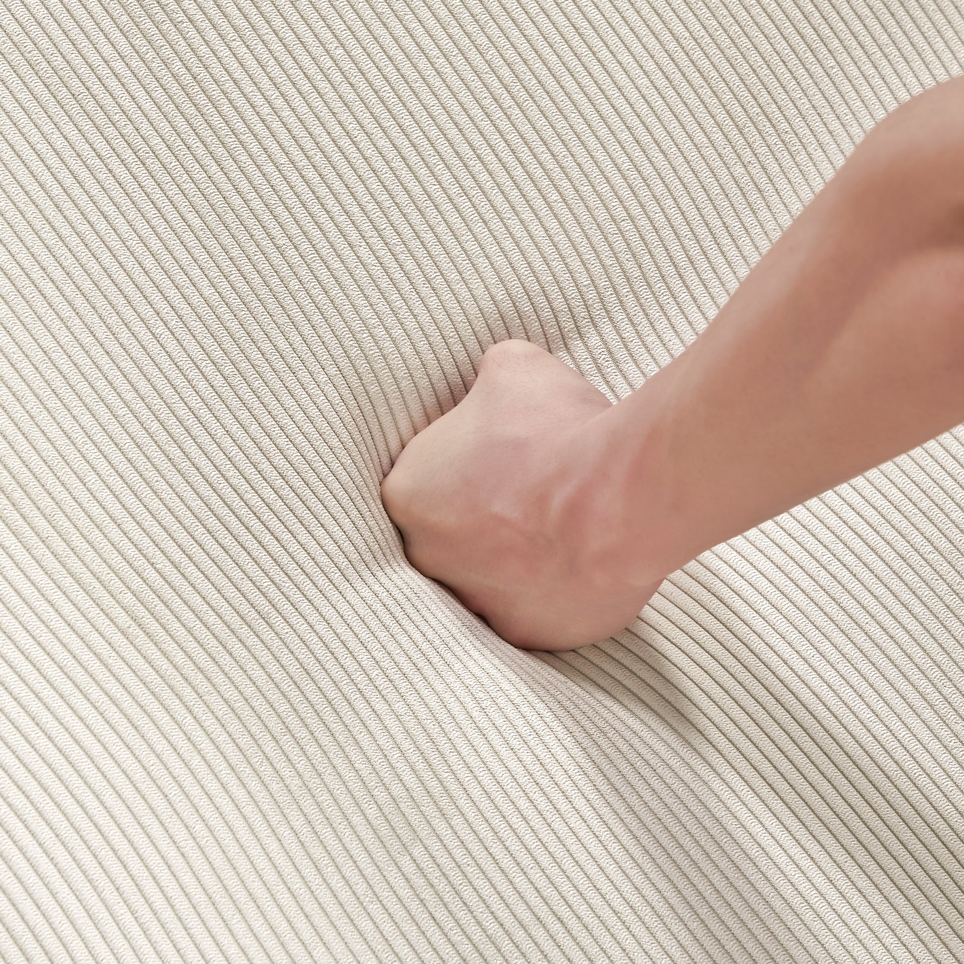 Closeup of a hand pressing into plush beige corduroy fabric showcasing its softness and texture