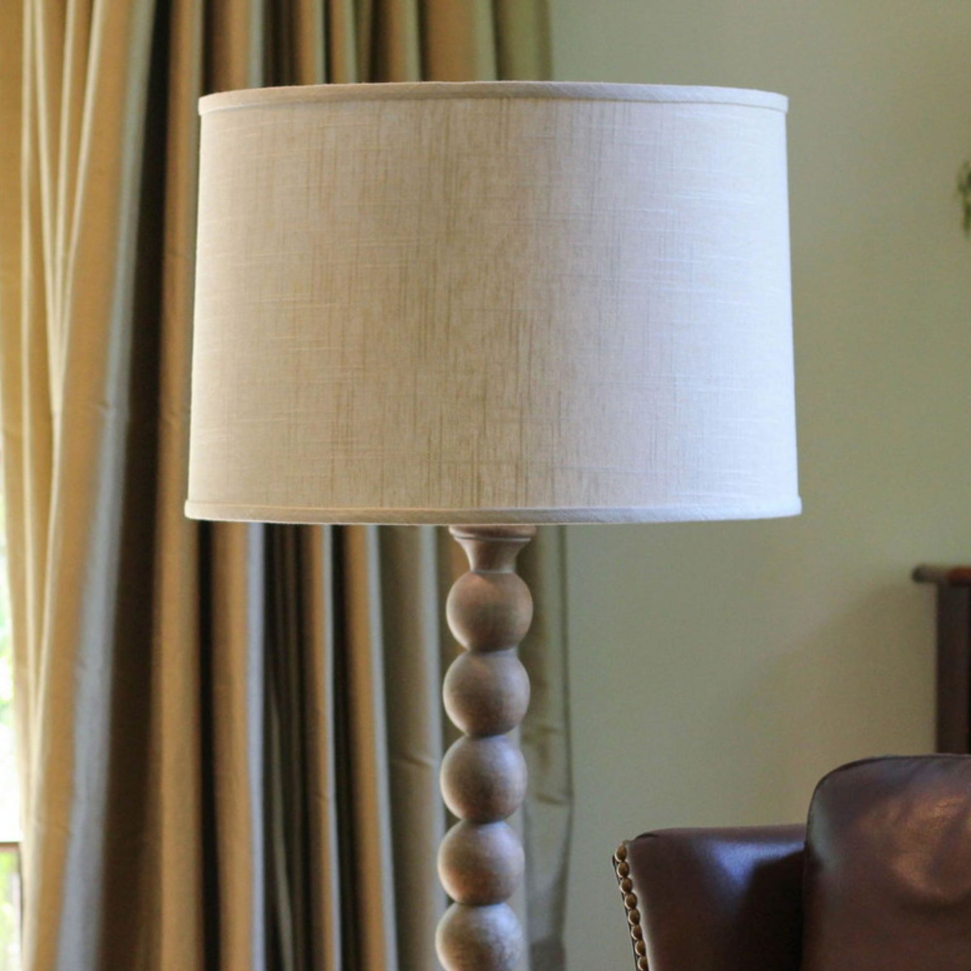 Textured linen drum lampshade with a decorative carved wood base and finial