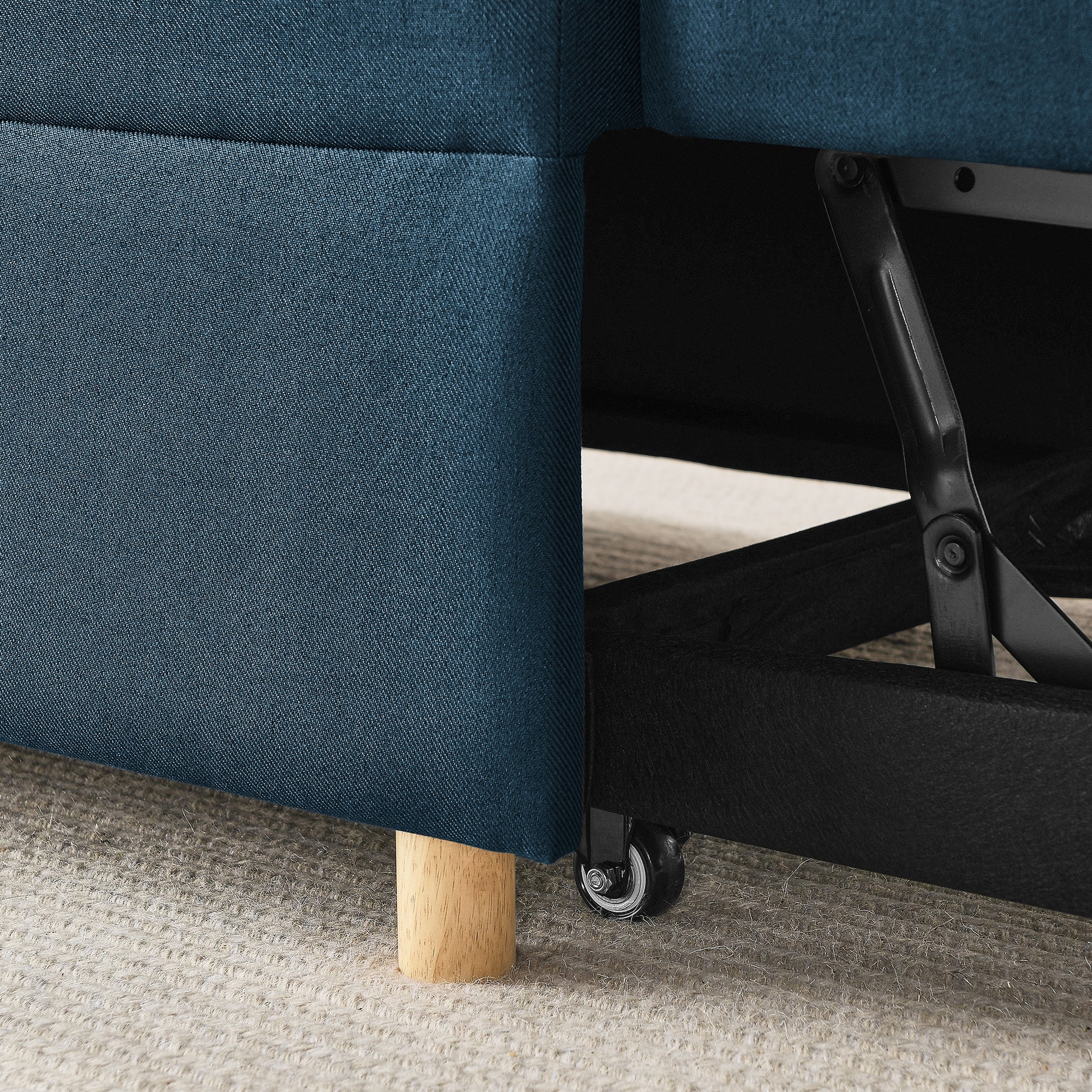 Closeup of dark blue fabric sofa featuring a hidden storage compartment mechanism with a wheel and wooden leg