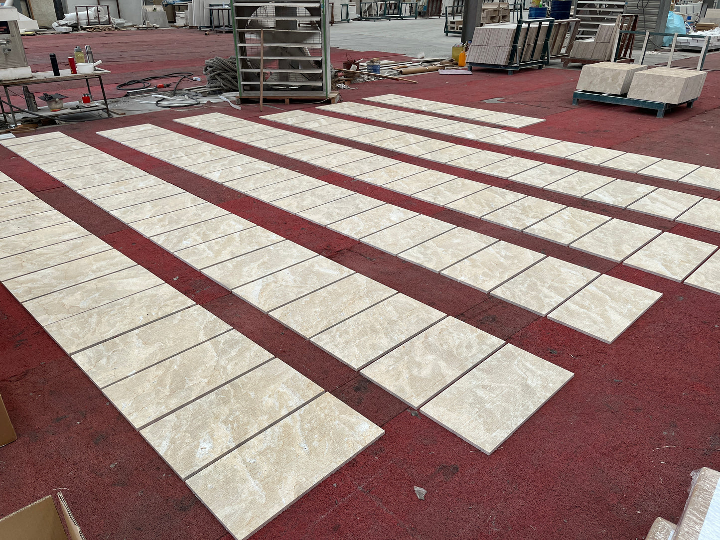 Beige travertine floor tiles laid in rows on a red carpet surface