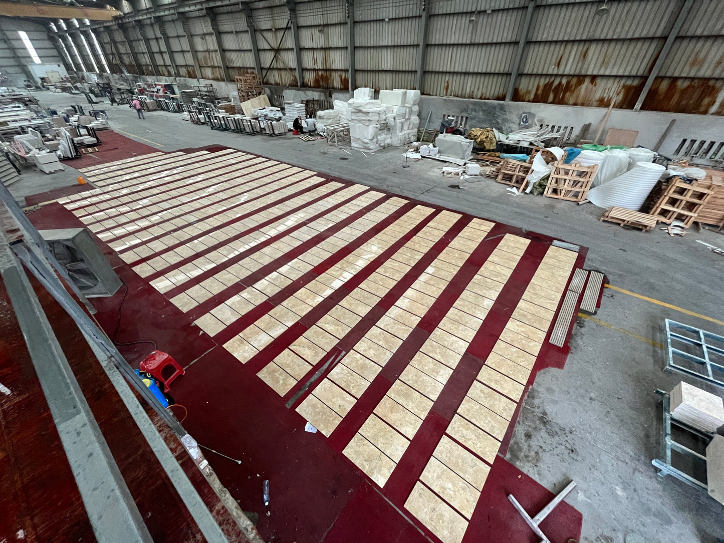 Rectangular beige marble tiles laid out in rows on a dark red surface ready for shipment