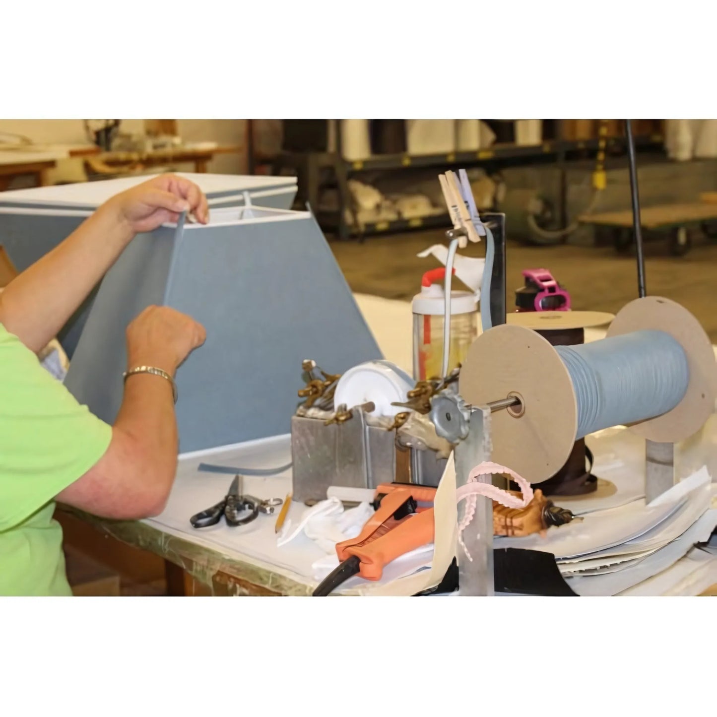 Gray fabric lampshade frame being assembled with tools and spools of thread nearby