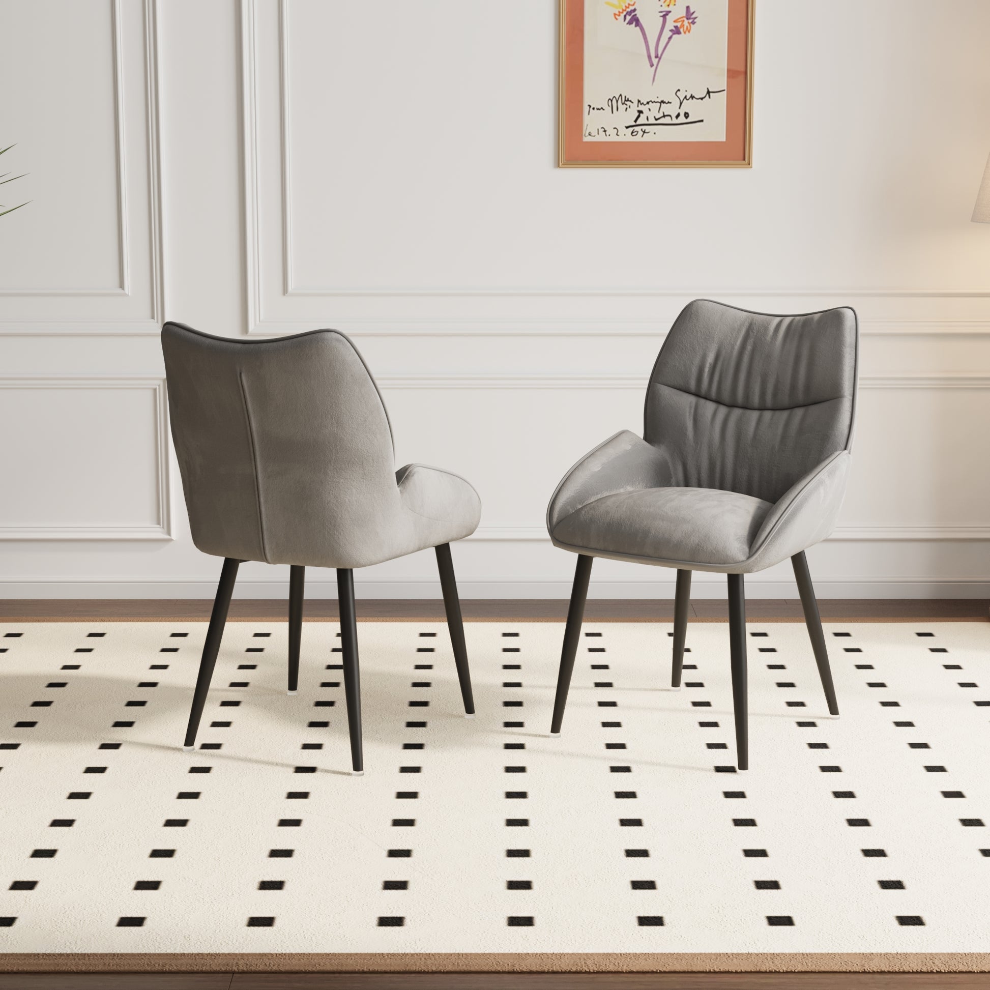 Two grey velvet accent chairs with black legs arranged on a cream rug with black diamond patterns