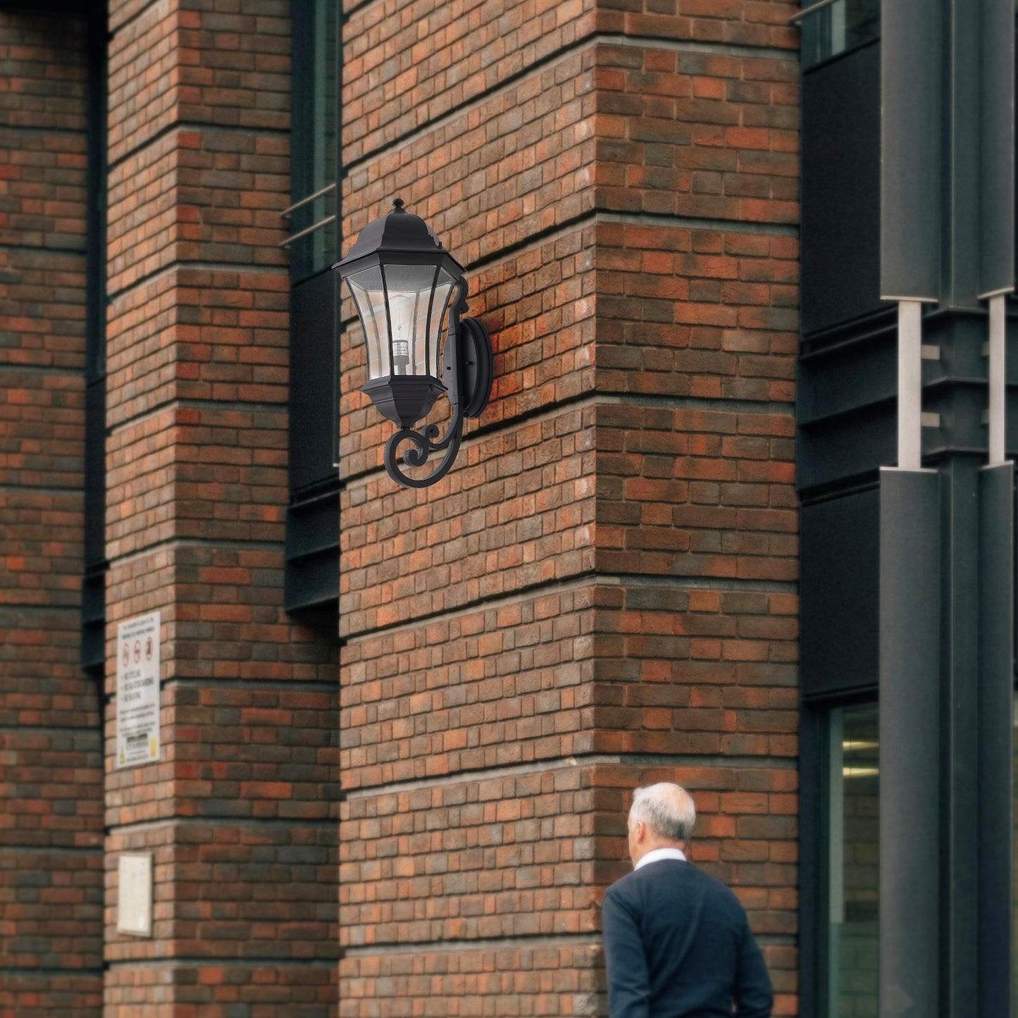 Black metal outdoor lantern with clear glass panels mounted on brick wall