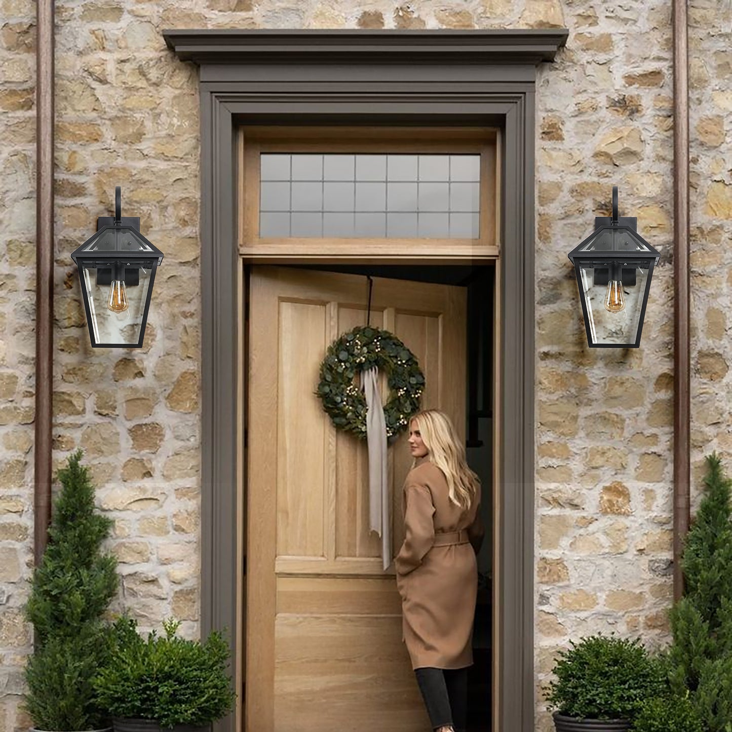 Black outdoor lantern with clear glass panes and a vintage Edison bulb mounted on a stone wall