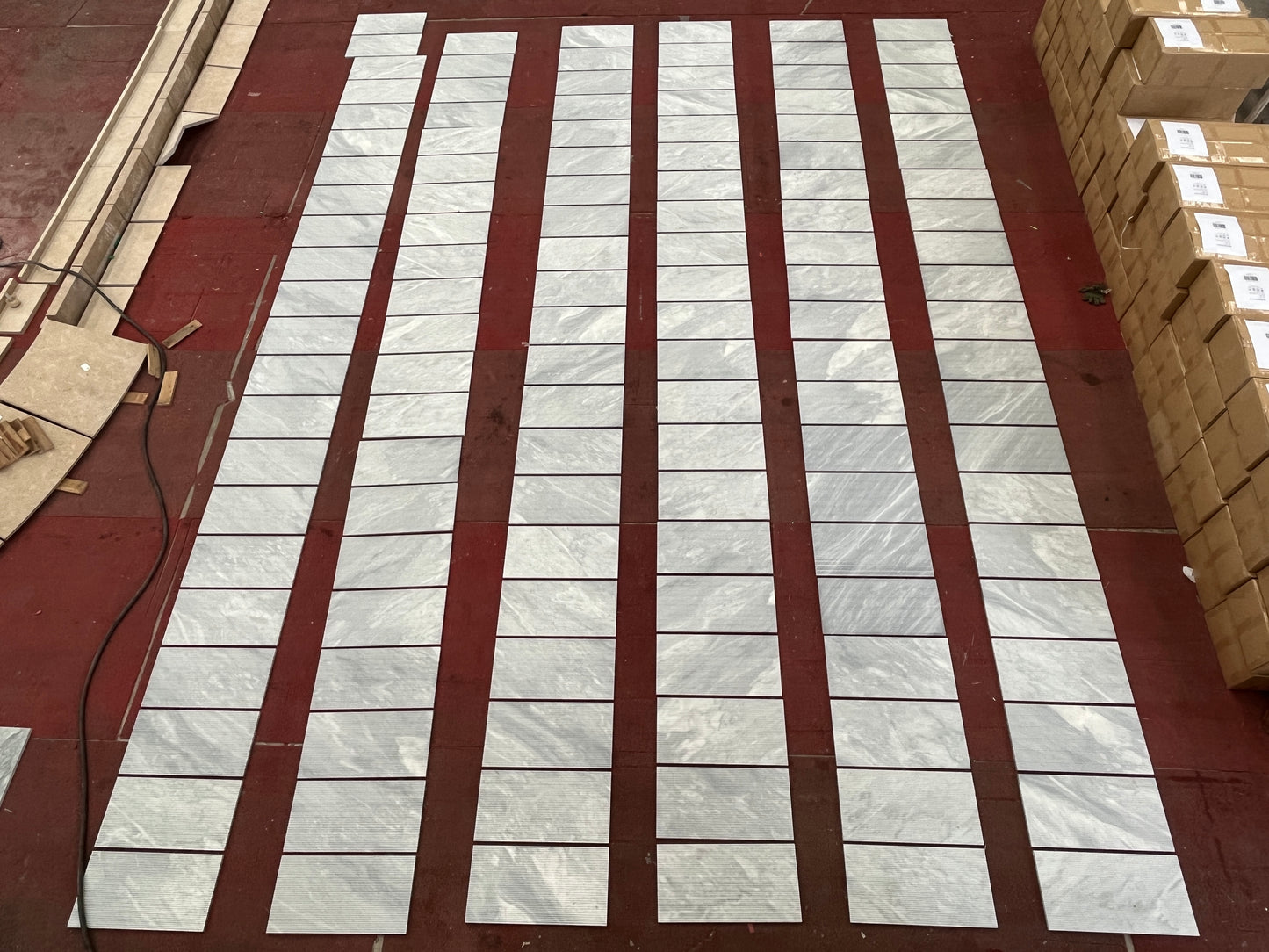 Light gray marble effect porcelain tiles laid out on a dark red floor