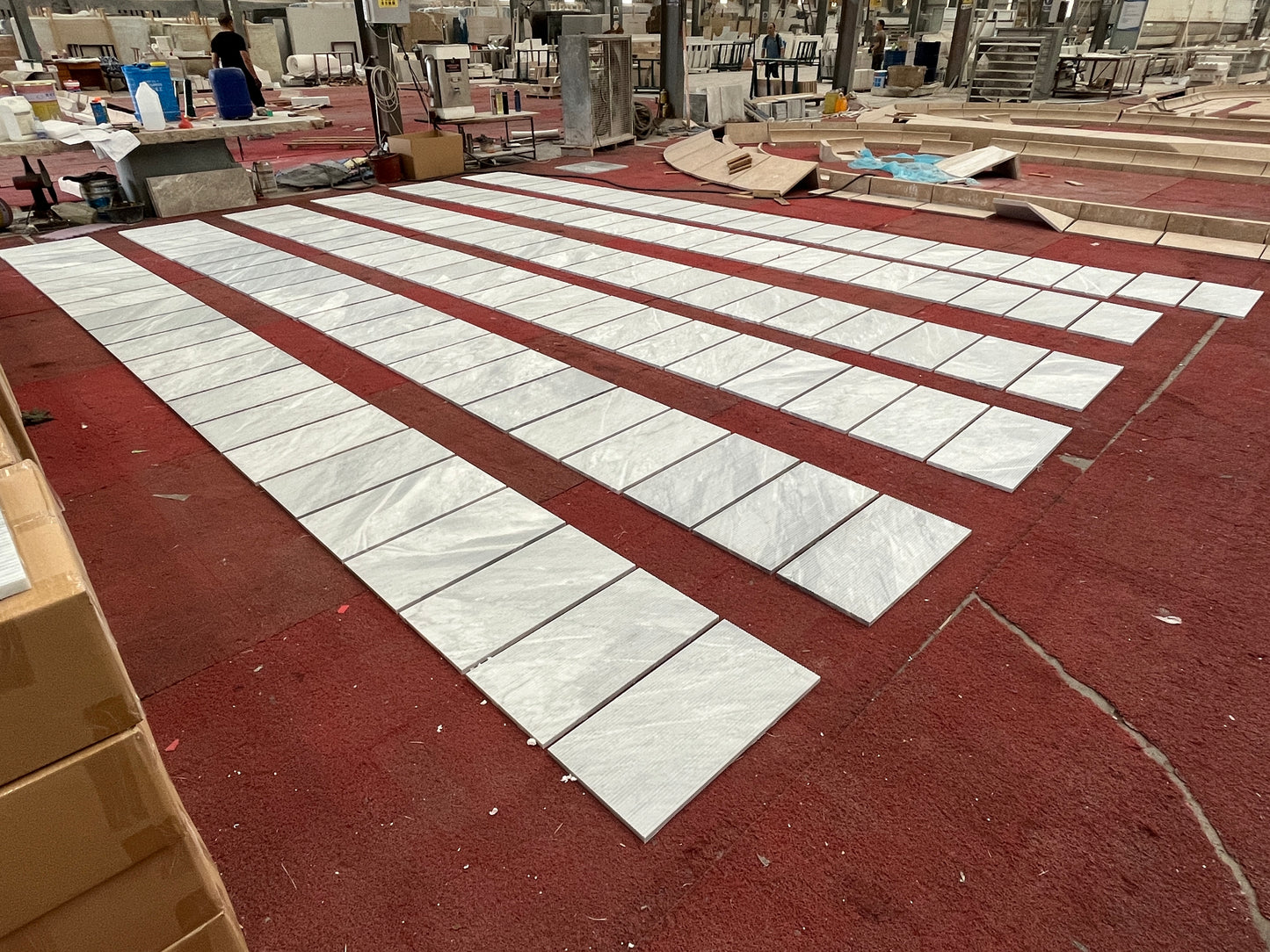 Light grey marble effect ceramic tiles laid out in rows on a red carpet floor