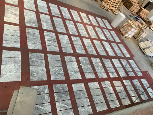Polished marble tiles with grey veining laid out on a dark red floor for inspection