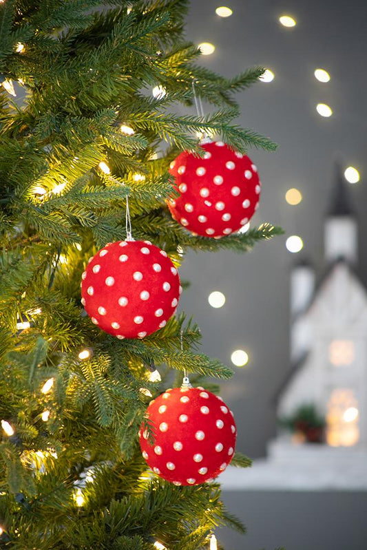 Red flocked polka dot Christmas ornament hanging on a decorated evergreen tree