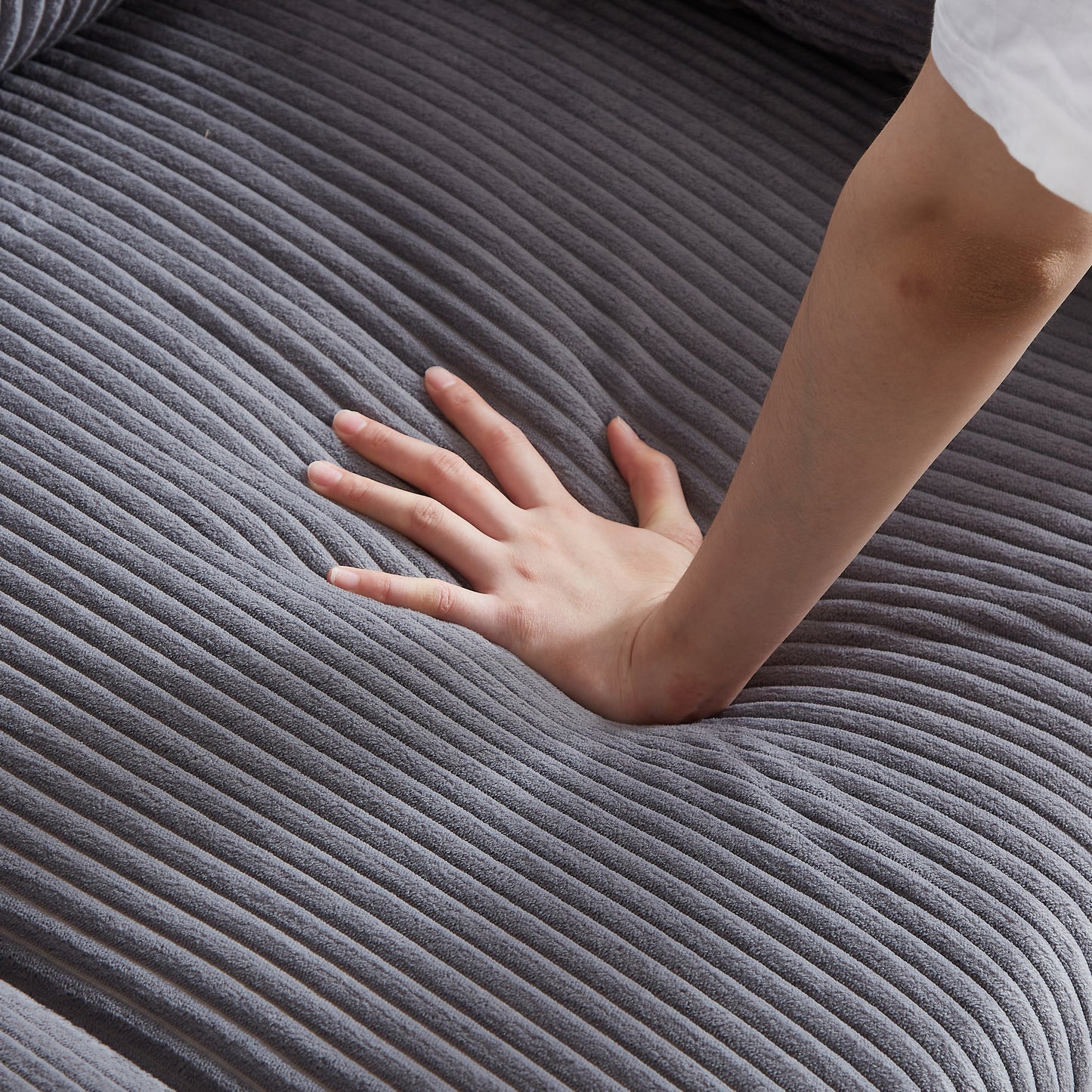 Closeup of plush grey corduroy fabric with a hand pressing into its soft texture for comfort