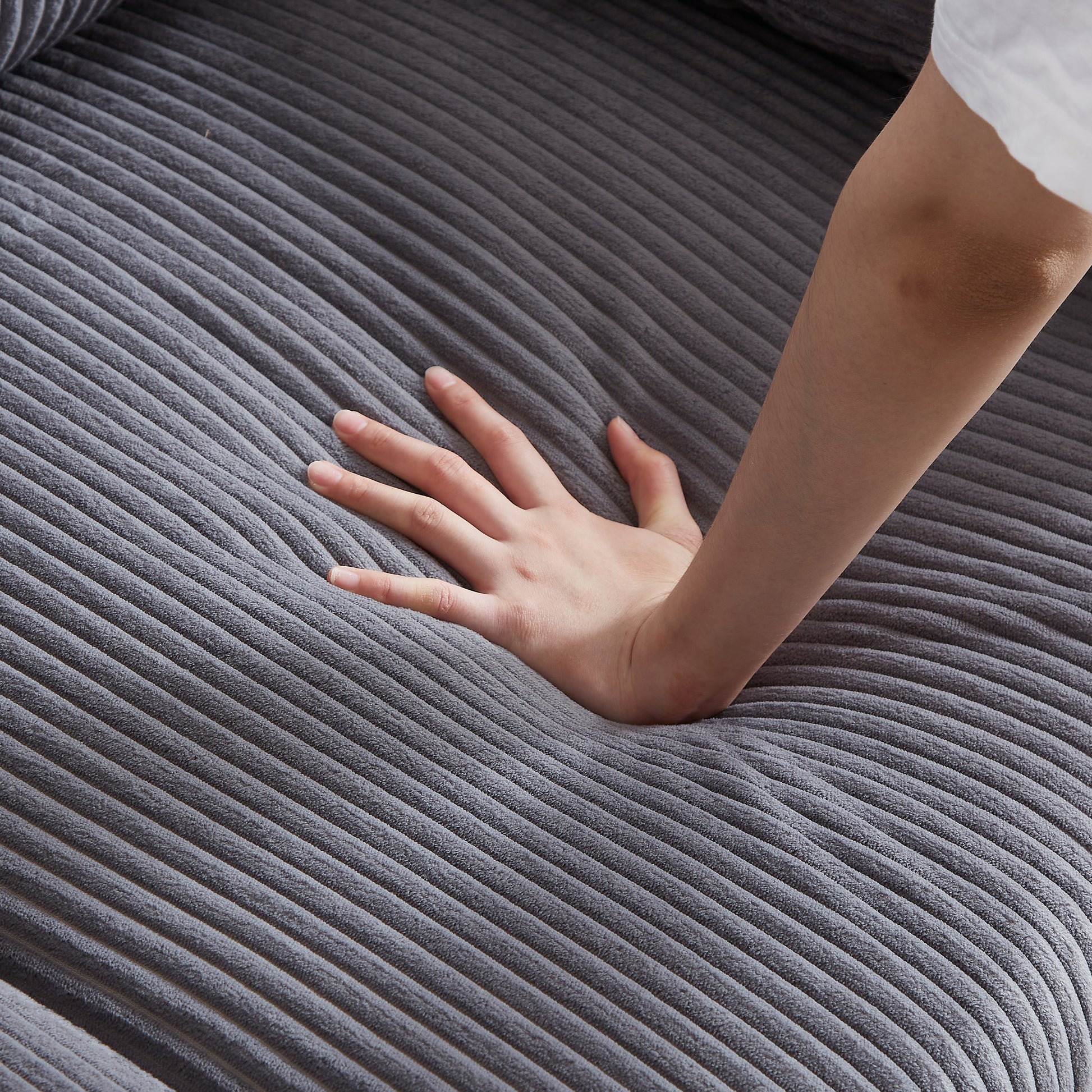 Closeup of plush grey corduroy fabric with a hand pressing into its soft texture for comfort