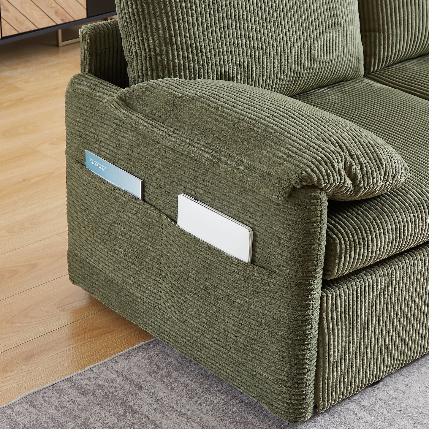 Olive green corduroy sofa armrest with integrated pockets holding a tablet and magazine