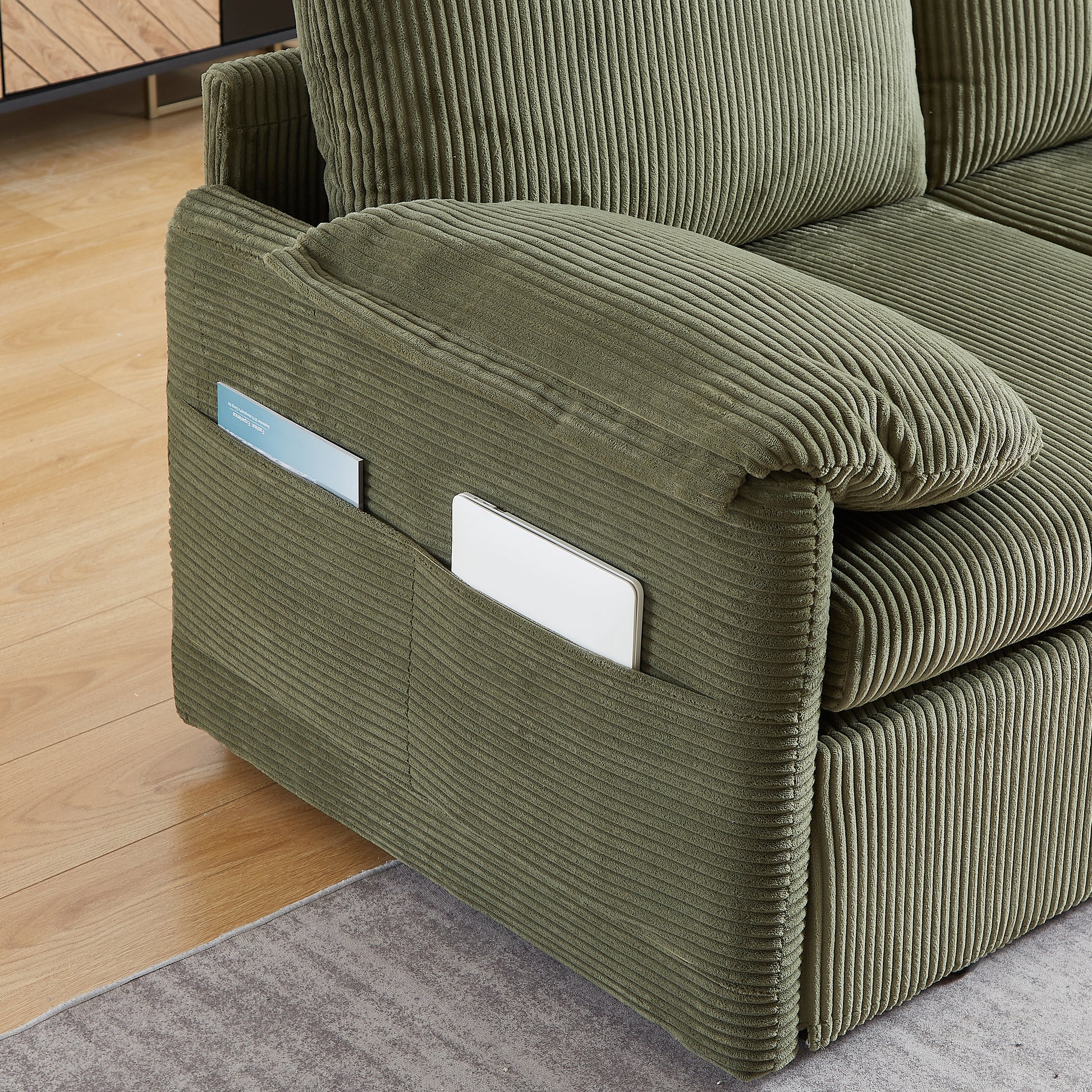 Olive green corduroy sofa armrest with integrated pockets holding a tablet and magazine