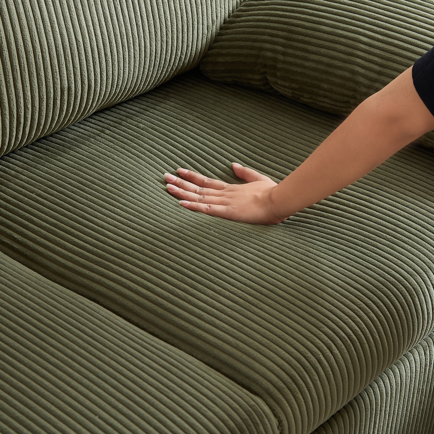 Closeup of plush olive green corduroy sofa fabric with a hand gently pressing the cushion