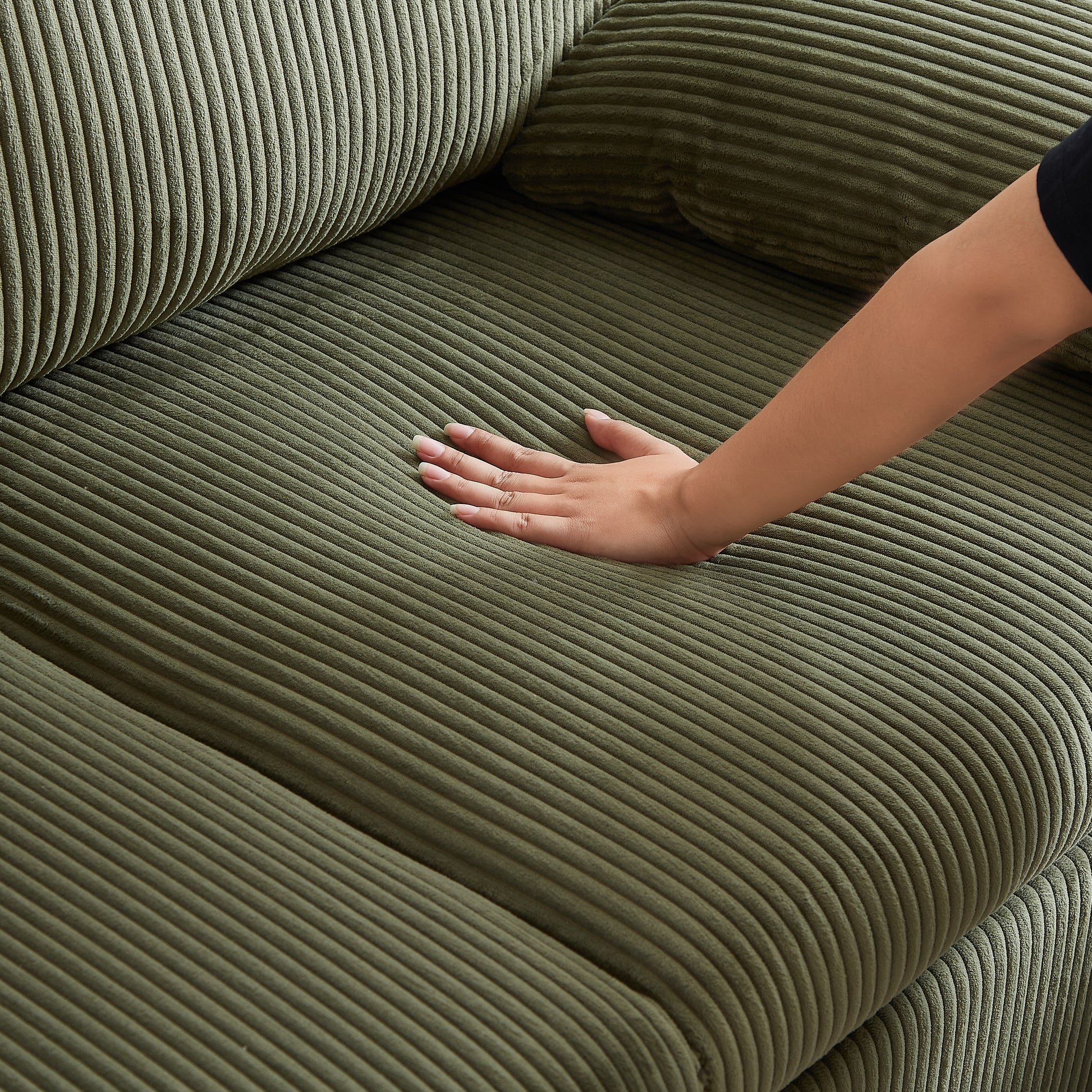 Closeup of plush olive green corduroy sofa fabric with a hand gently pressing the cushion