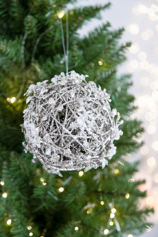 Glittery silver orb Christmas ornament with icelike accents hanging on a green tree