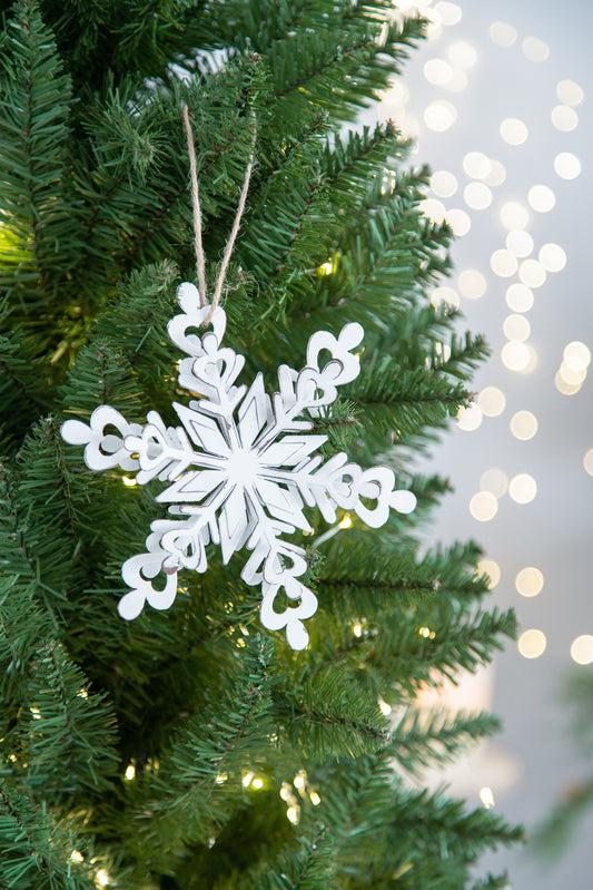 White wooden snowflake ornament hanging on a green Christmas tree with bokeh lights