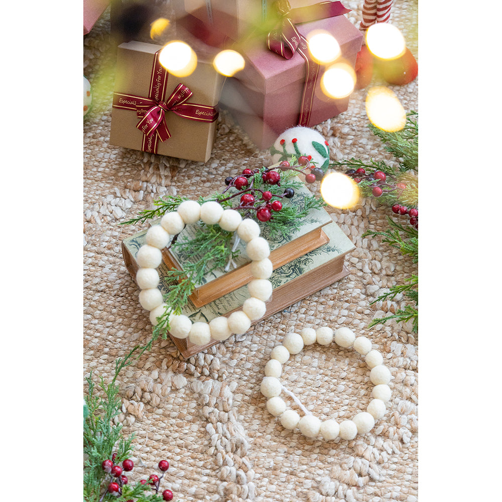 Two cream felt ball garlands draped on rustic woven rug with holiday gifts