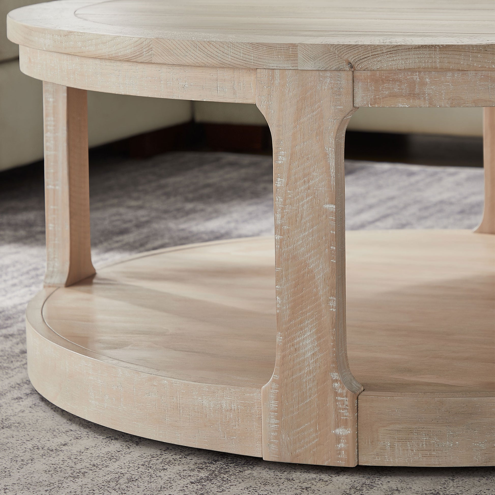 Round whitewashed wood coffee table with a lower shelf and carved legs
