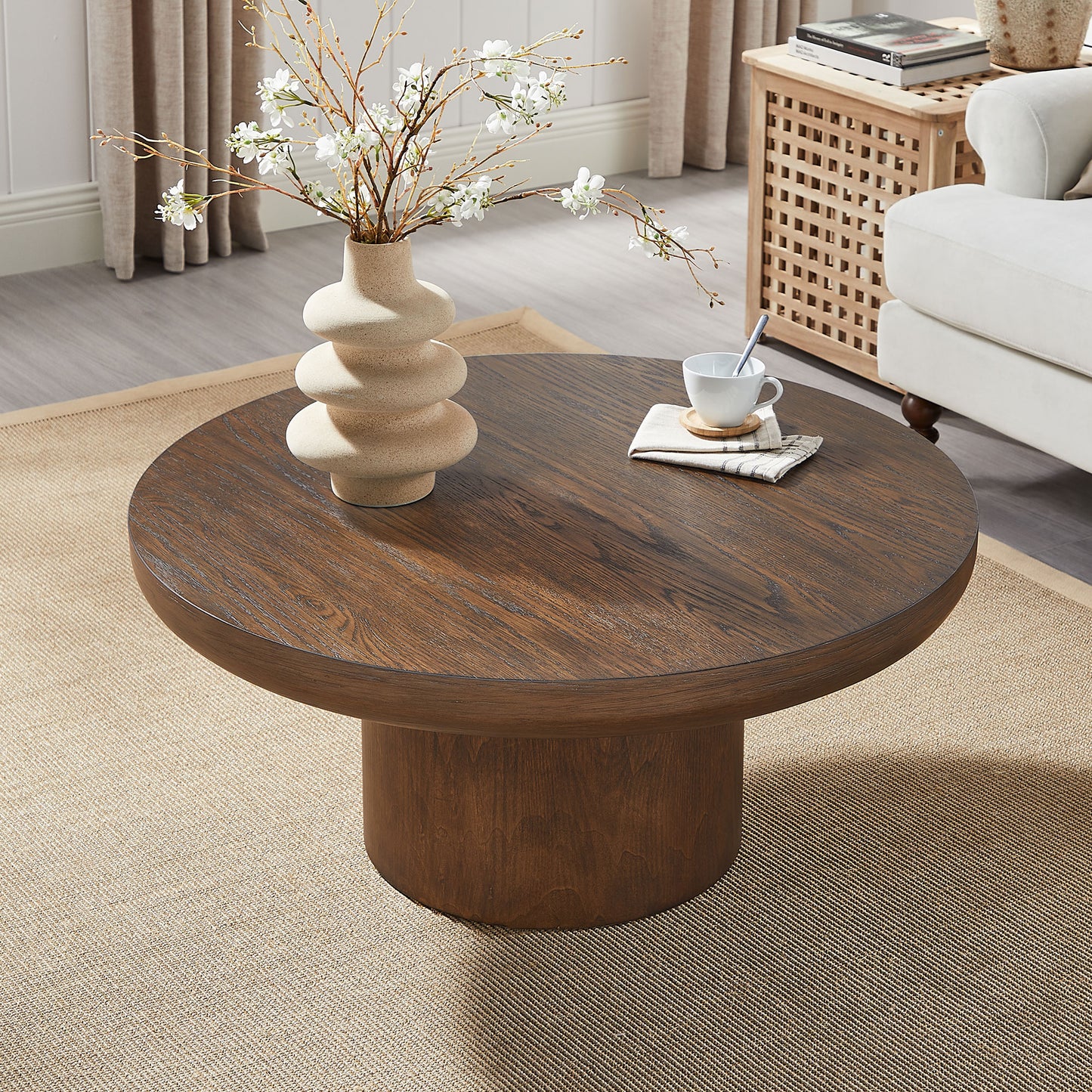 Round dark wood coffee table with a modern pedestal base and textured vase