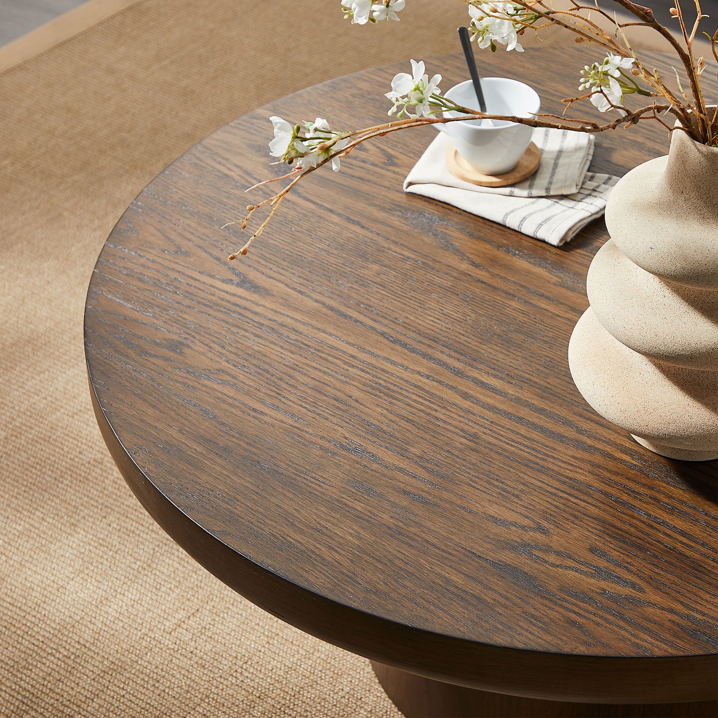 Dark oak wood round coffee table with textured ceramic vase and white flowers