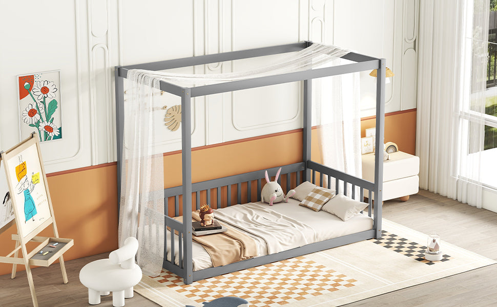 Gray wooden canopy bed frame with sheer drapes and toddler bedding