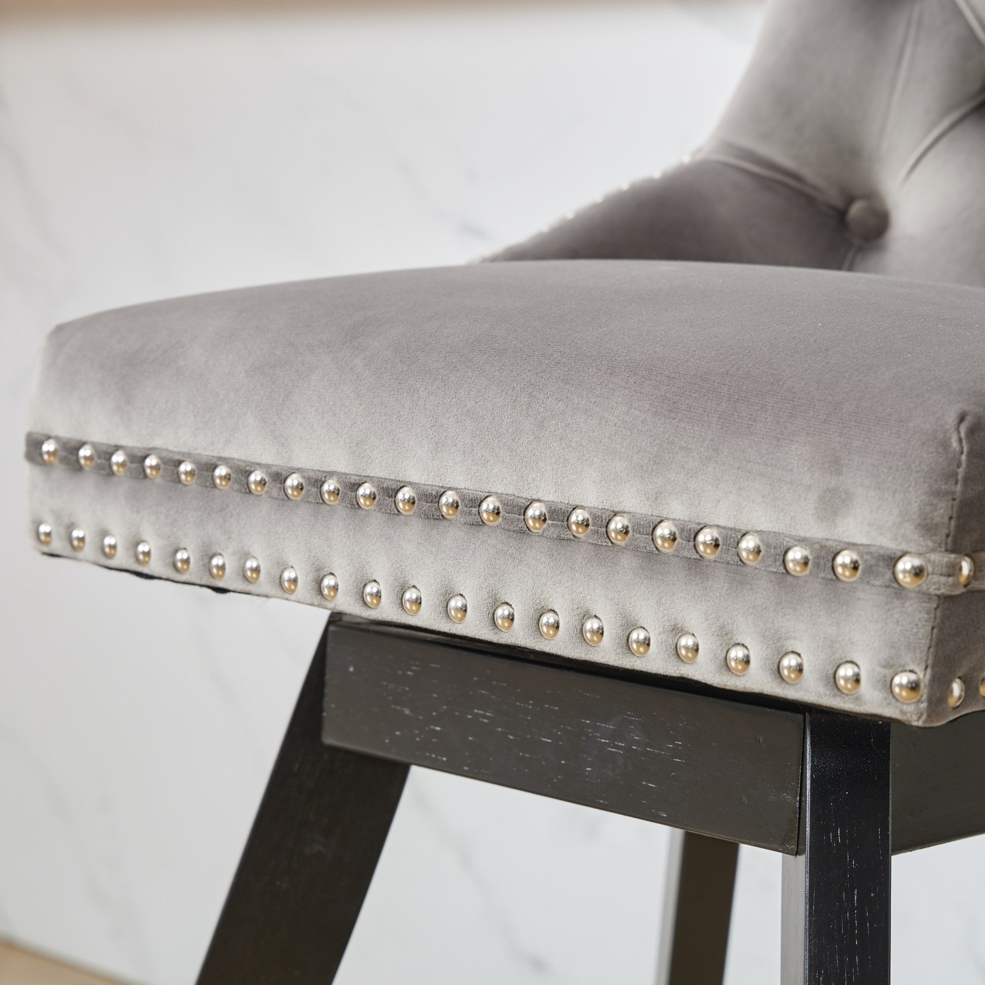 Grey velvet bar stool with decorative silver nailhead trim and dark wood legs