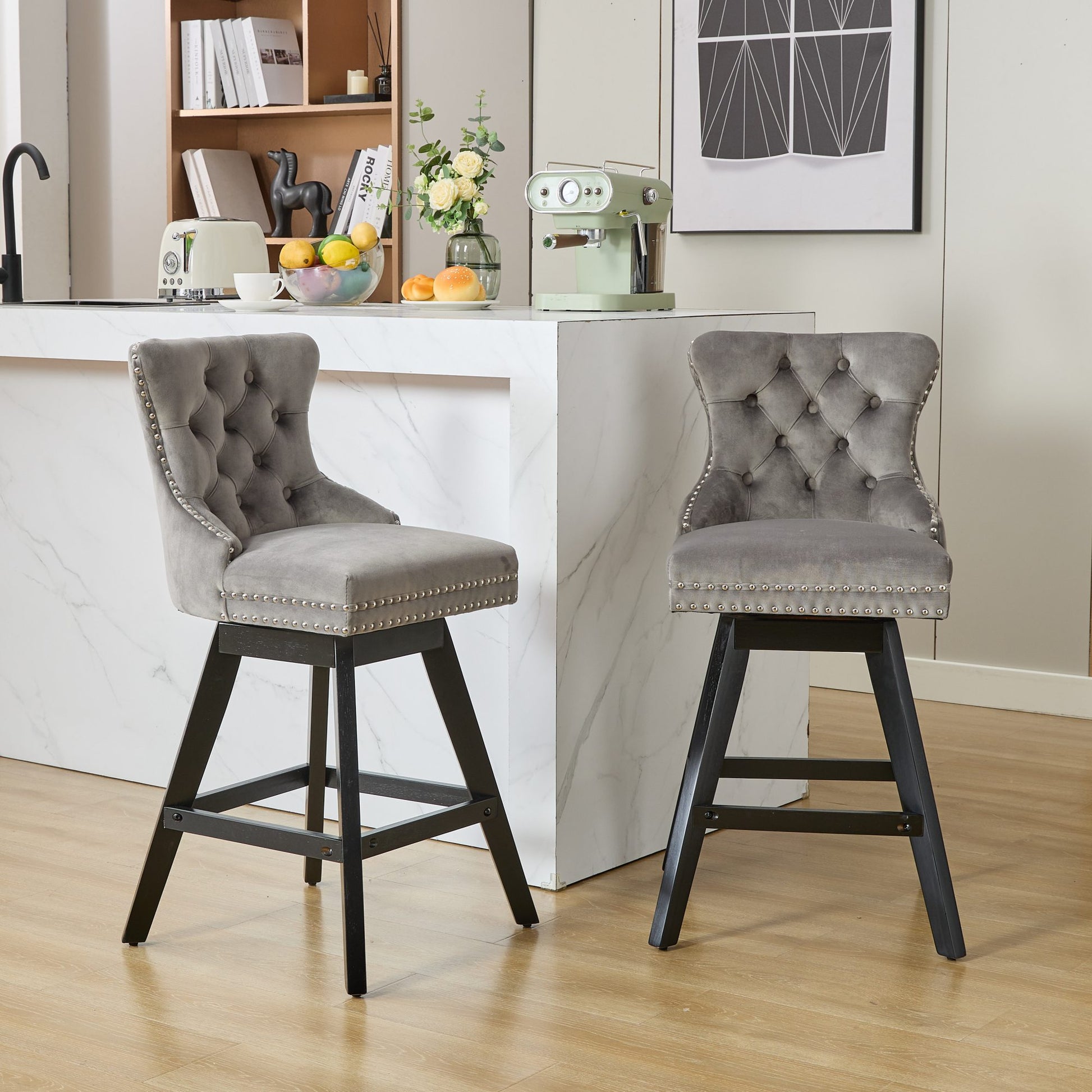 Two grey velvet bar stools with tufted backs and silver nailhead trim featuring swivel seats and black wooden legs perfect for a modern kitchen island