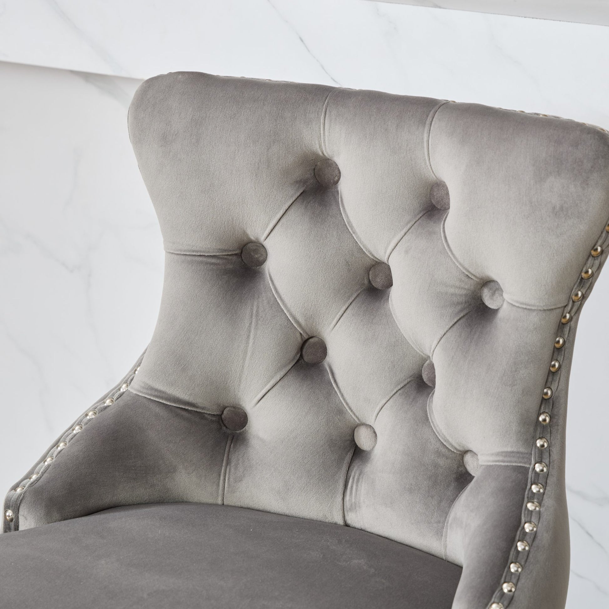 Closeup of a tufted grey velvet accent chair with silver nailhead trim