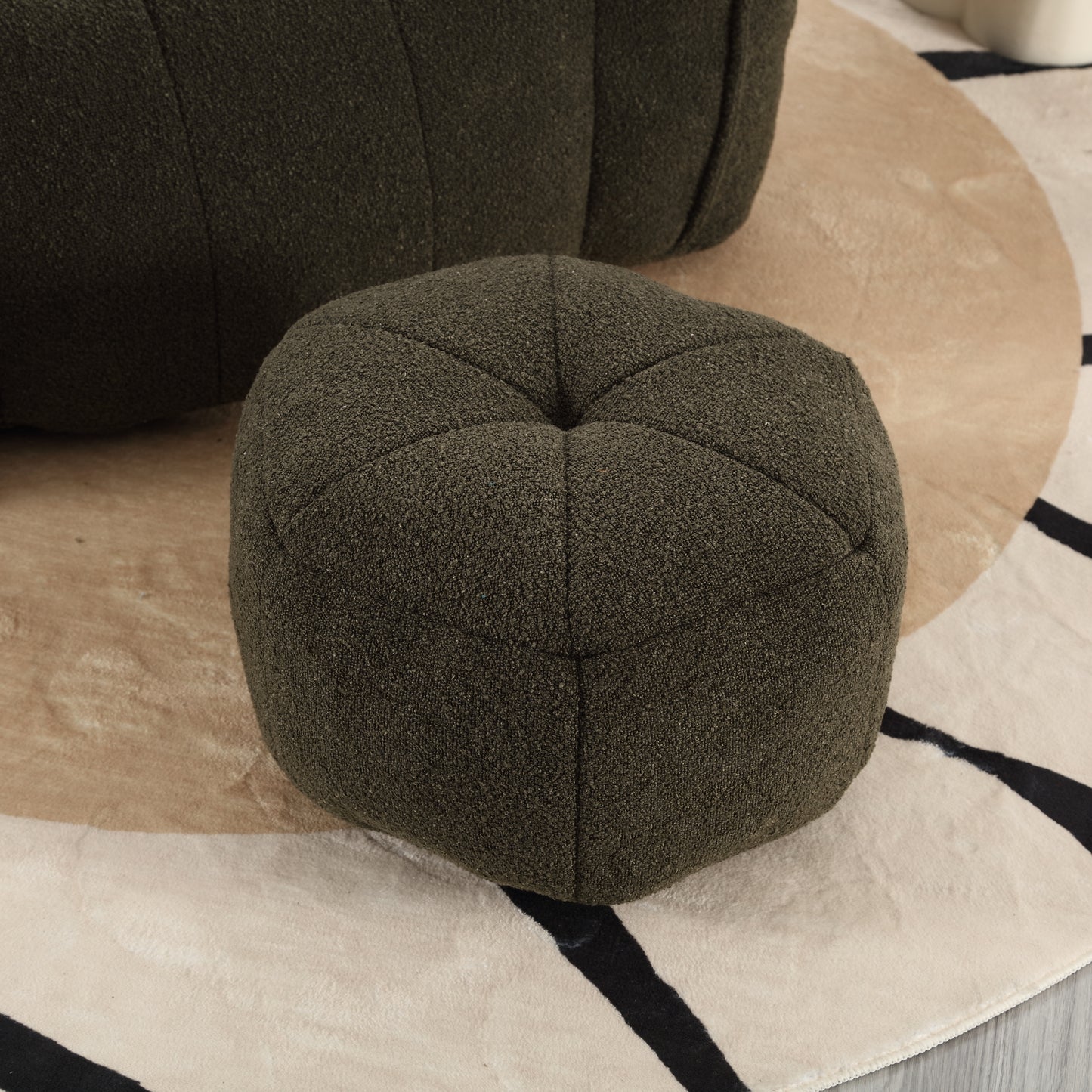 Dark green textured fabric pouf with tufted top on a patterned rug