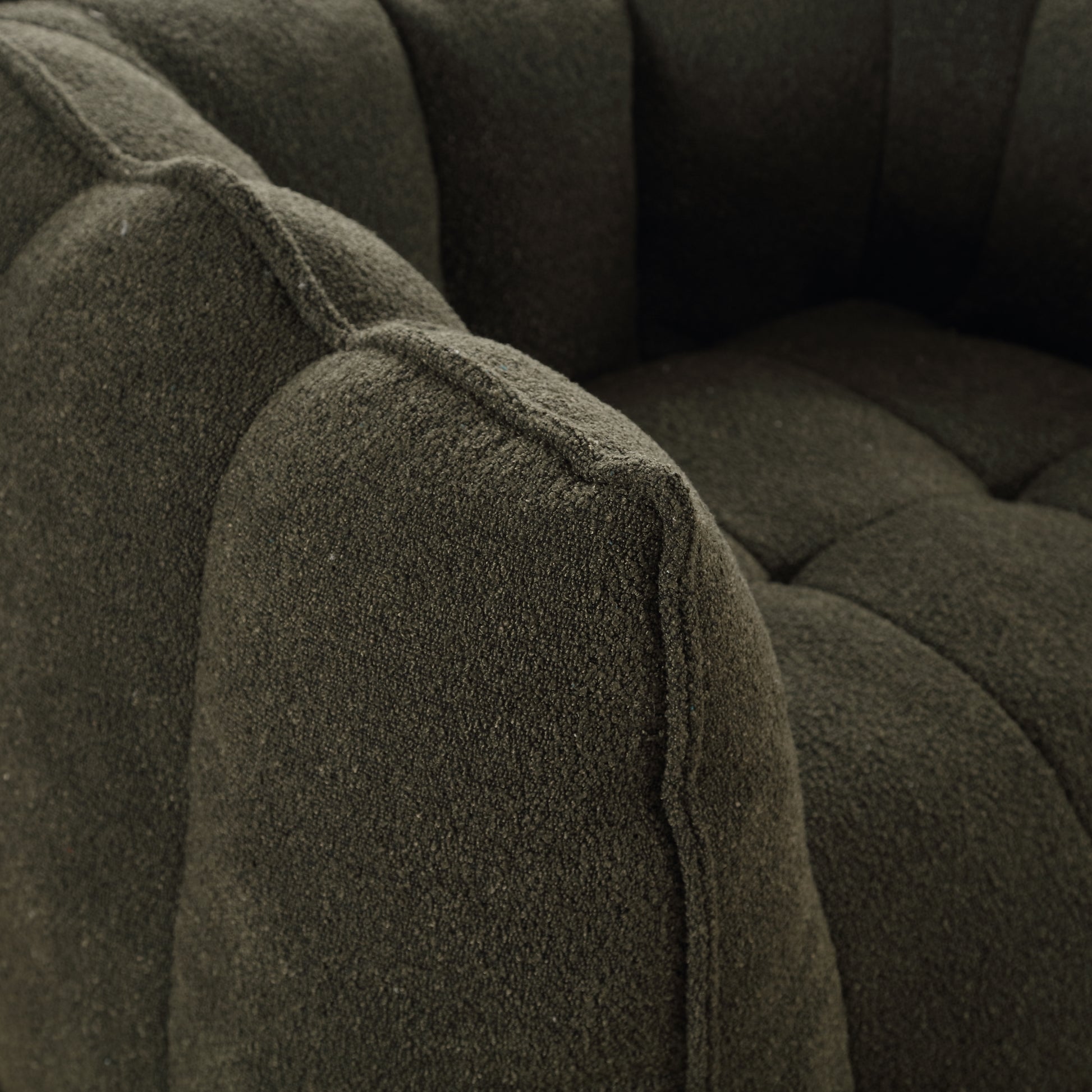 Closeup of a dark green textured boucle fabric on a modern armchair armrest