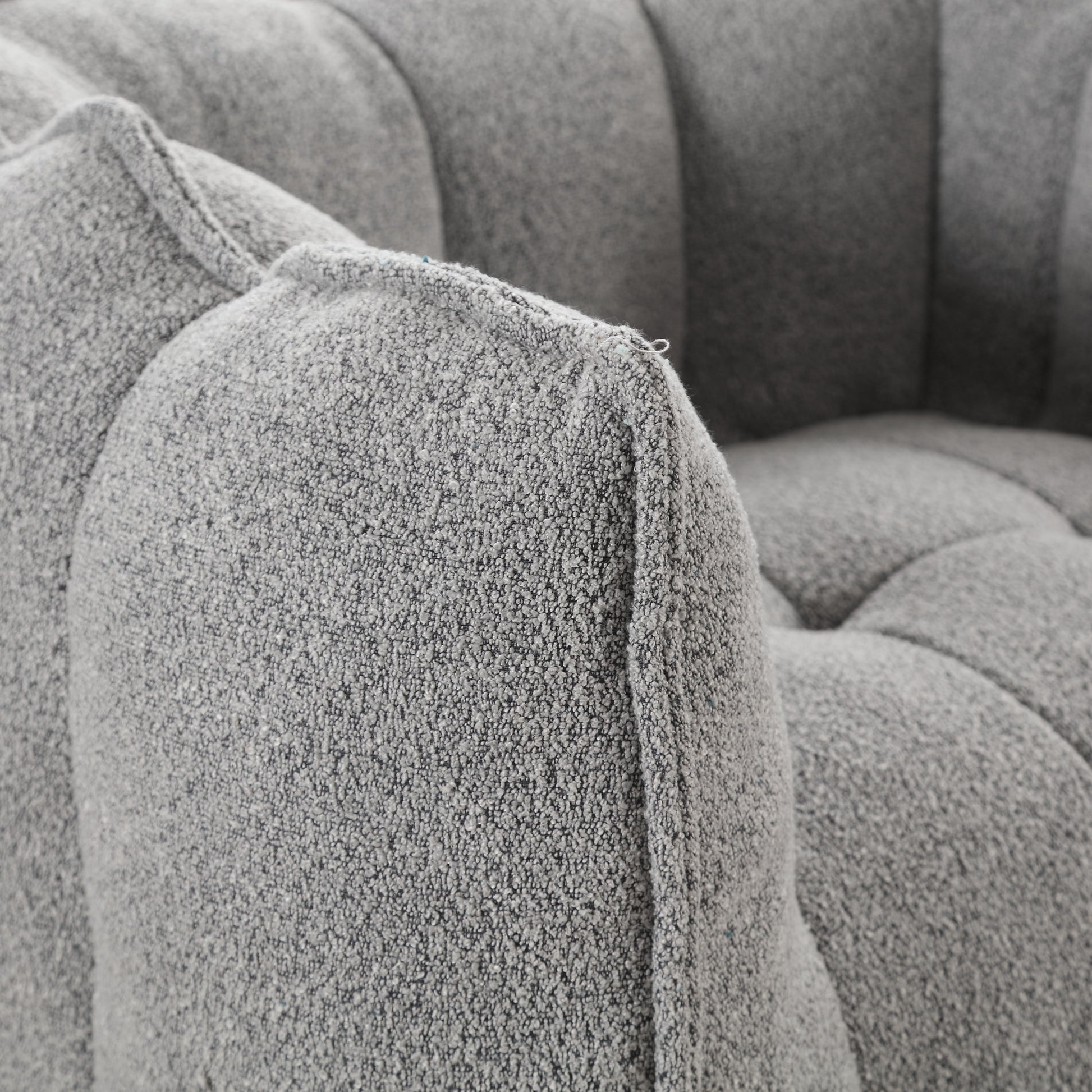 Closeup of a grey boucle armchair armrest with detailed textured fabric