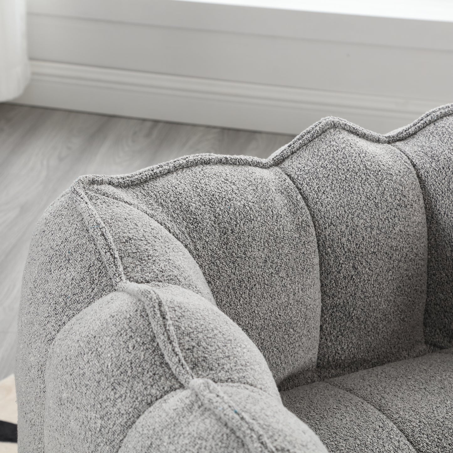 Closeup of a grey boucle armchair with deep tufting and stitched details