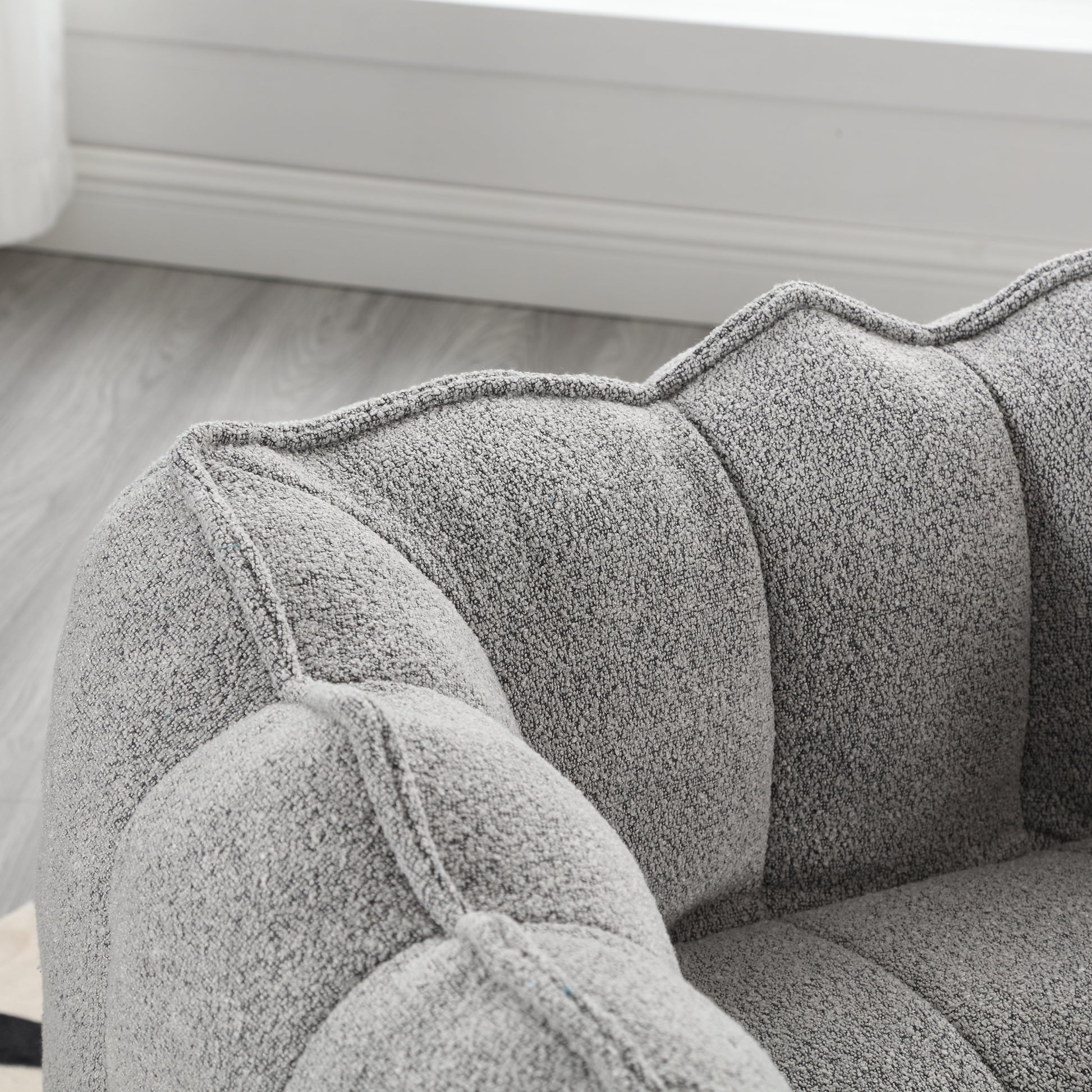 Closeup of a grey boucle armchair with deep tufting and stitched details