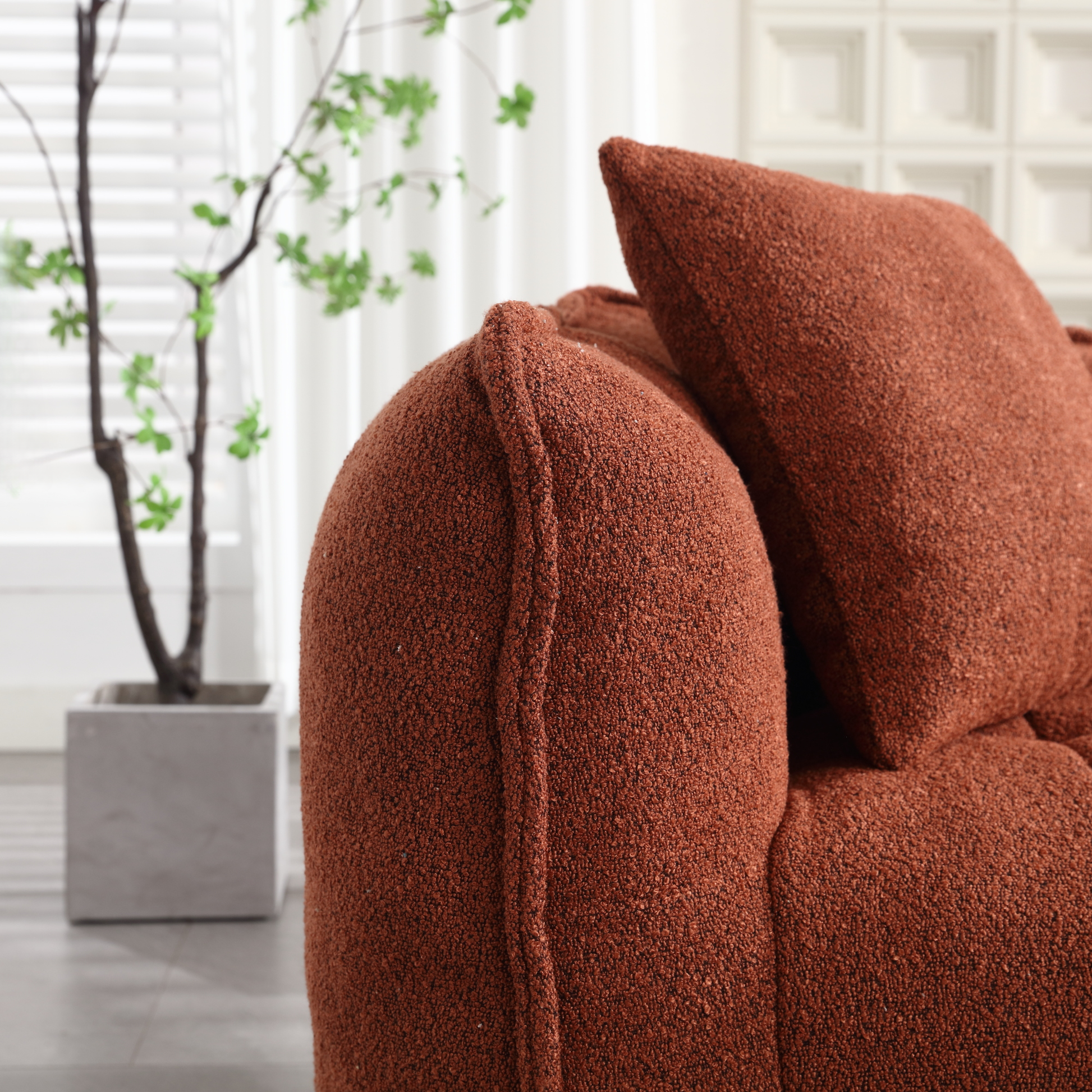 Closeup of a rustcolored boucle fabric sofa arm with textured detailing and matching throw pillow
