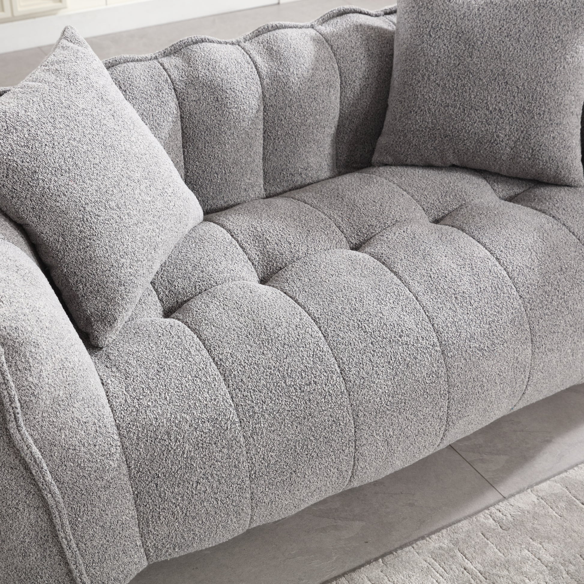 Tufted grey boucl sofa with plush throw pillows for a cozy living room