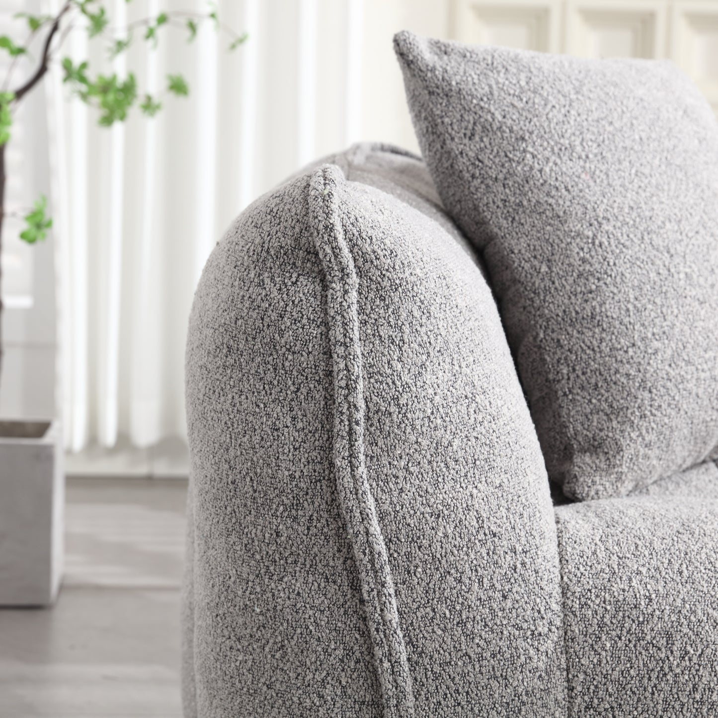 Closeup of a textured grey boucle sofa arm with a matching cushion behind