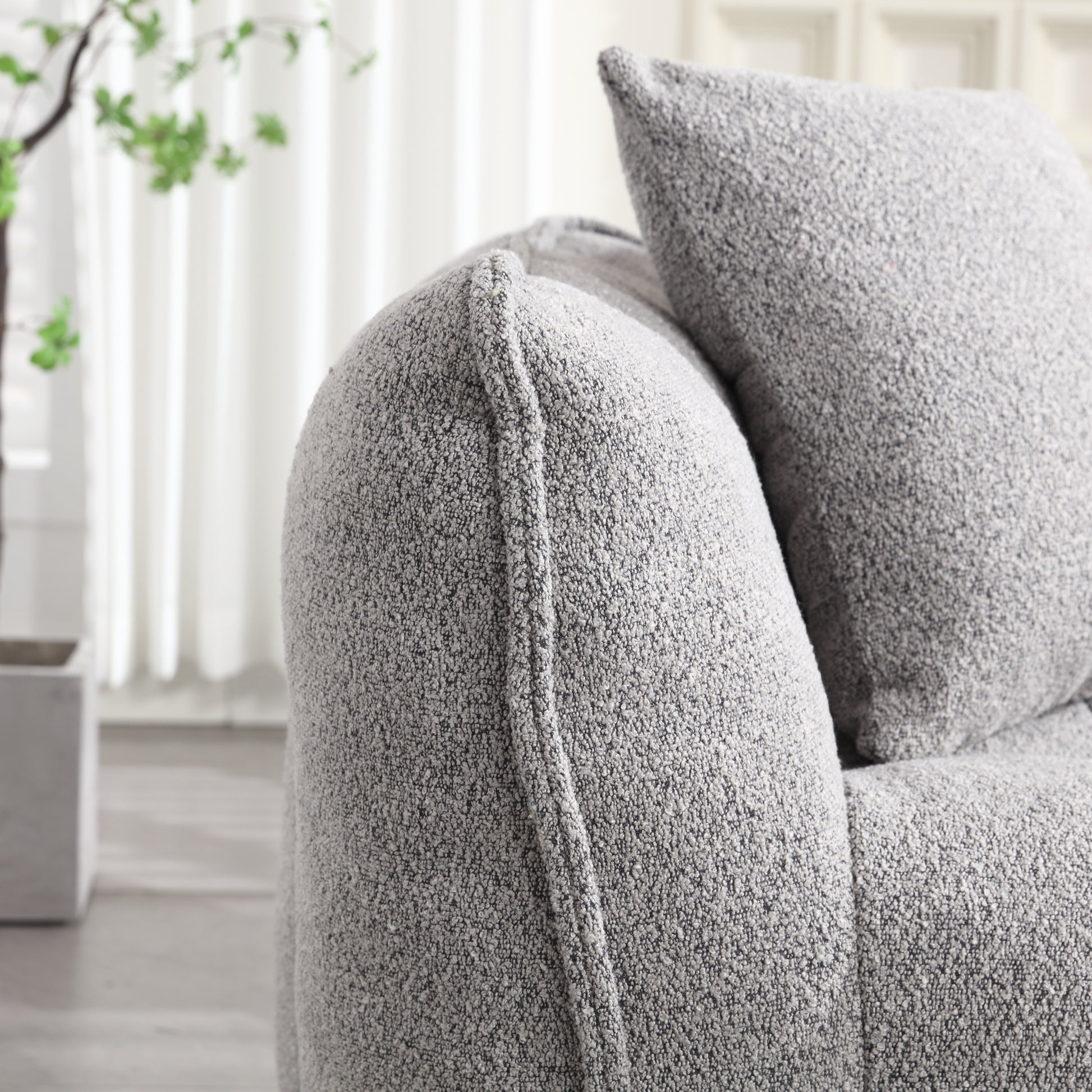 Closeup of a textured grey boucle sofa arm with a matching cushion behind