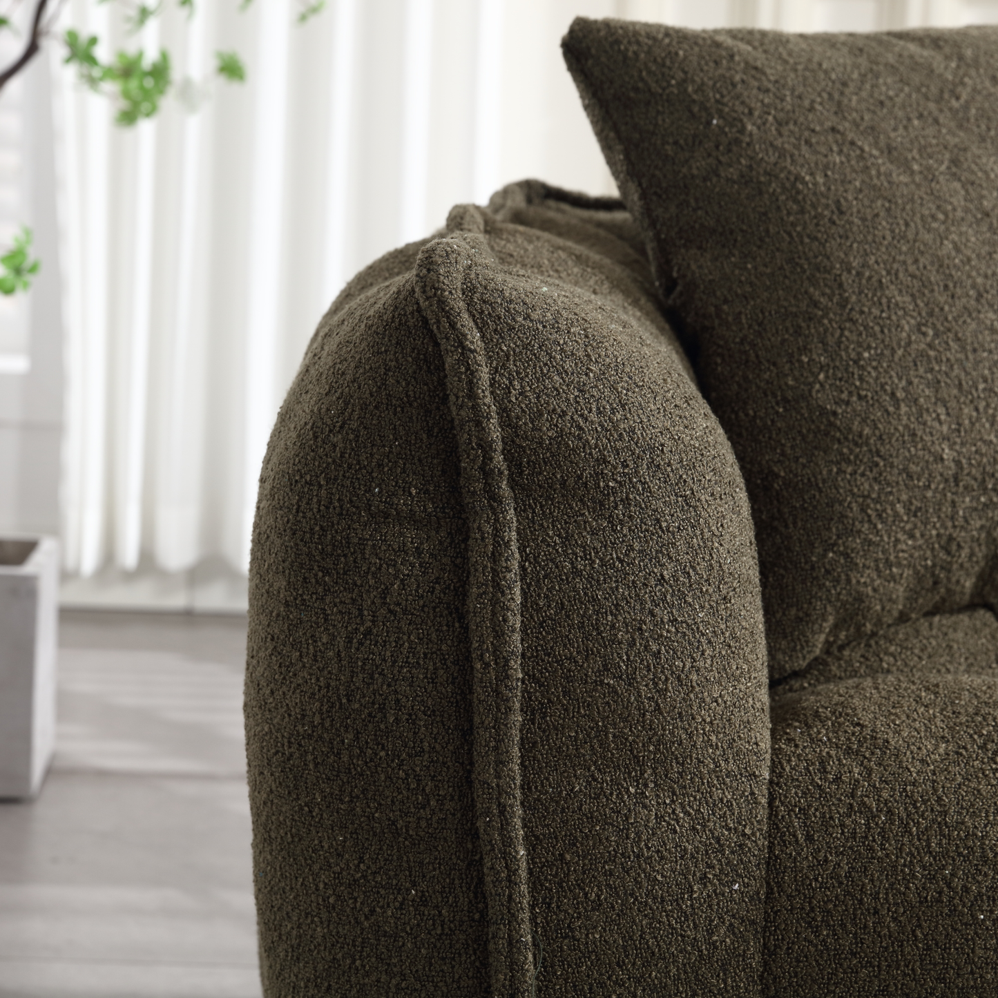 Closeup of a textured dark green boucle fabric sofa arm with detailed stitching
