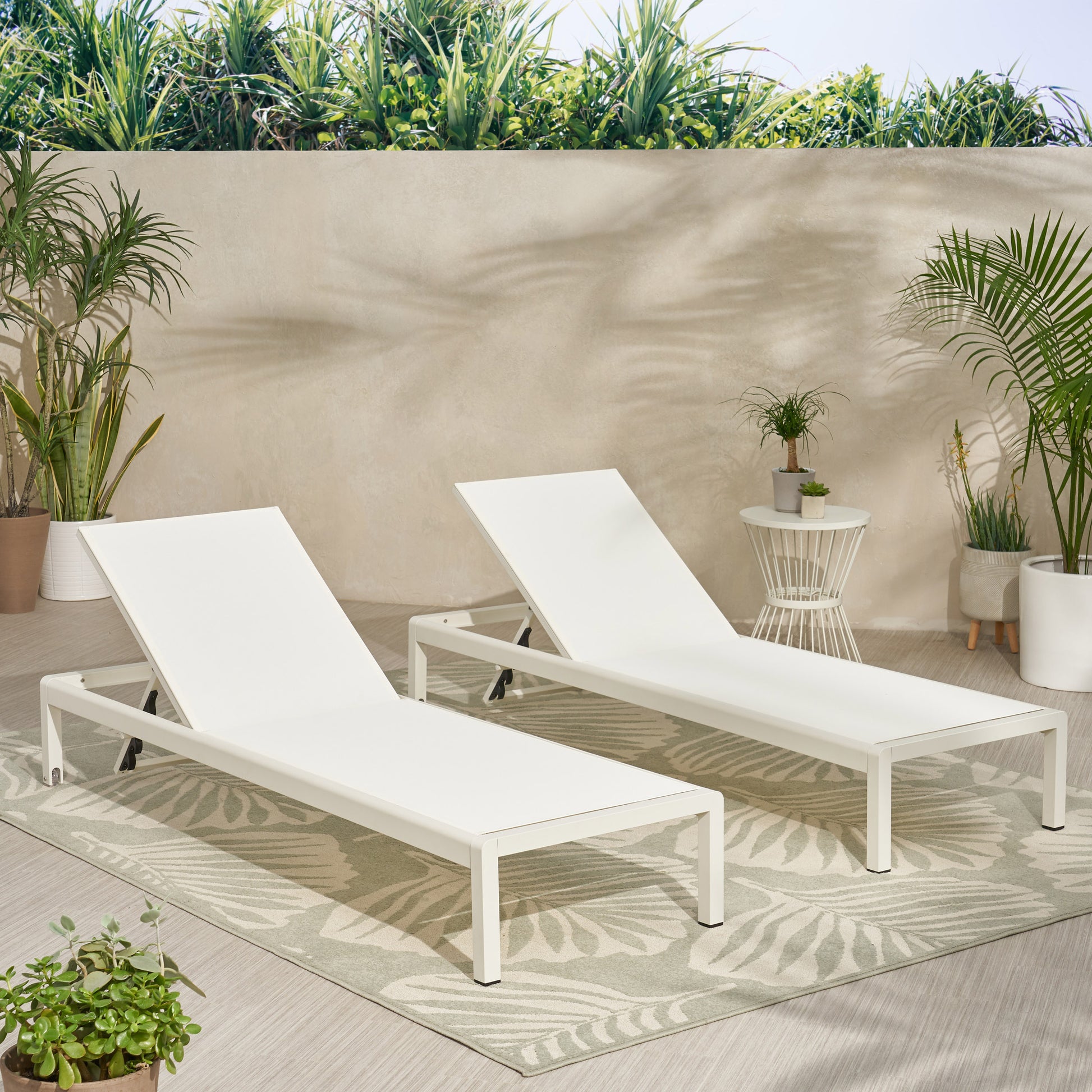 Two white aluminum lounge chairs with adjustable backrests on a palm leaf patterned rug