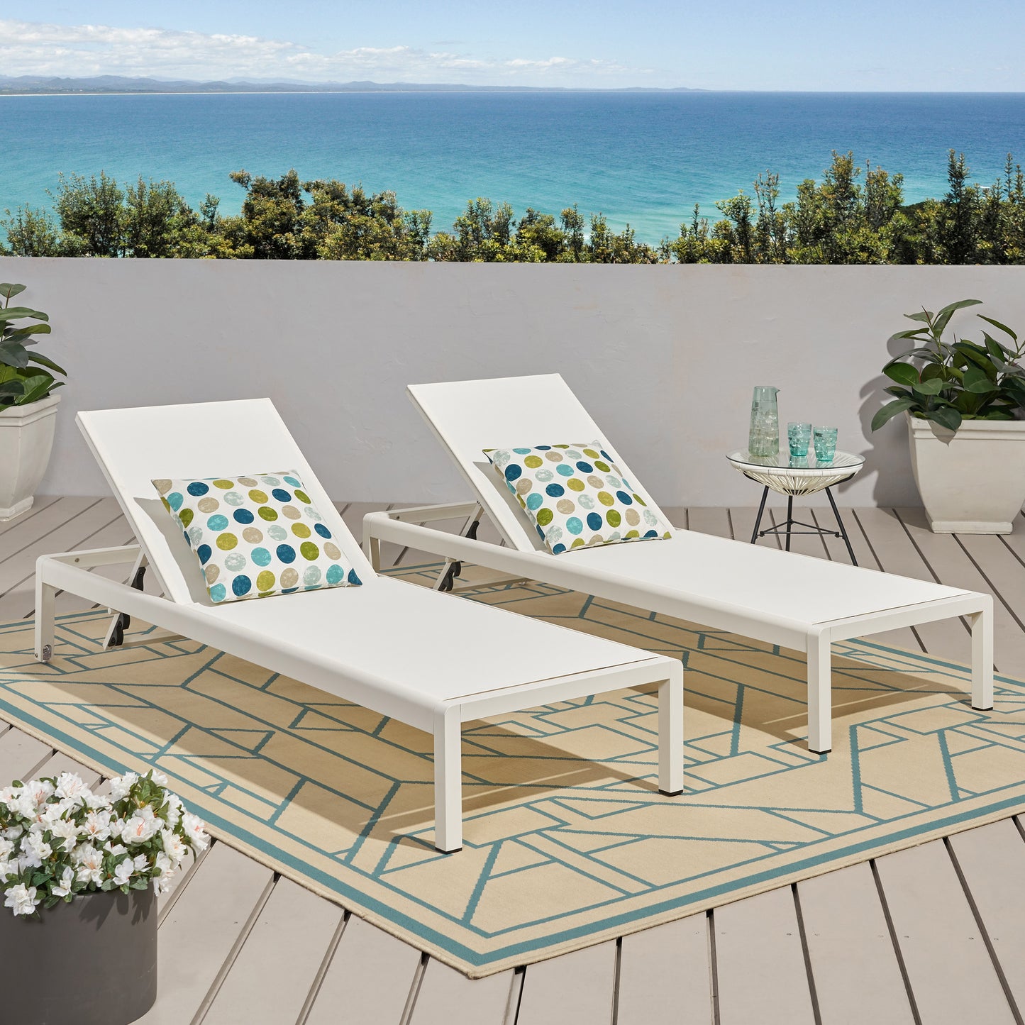 Two white aluminum chaise lounges with colorful patterned pillows on a deck overlooking the ocean