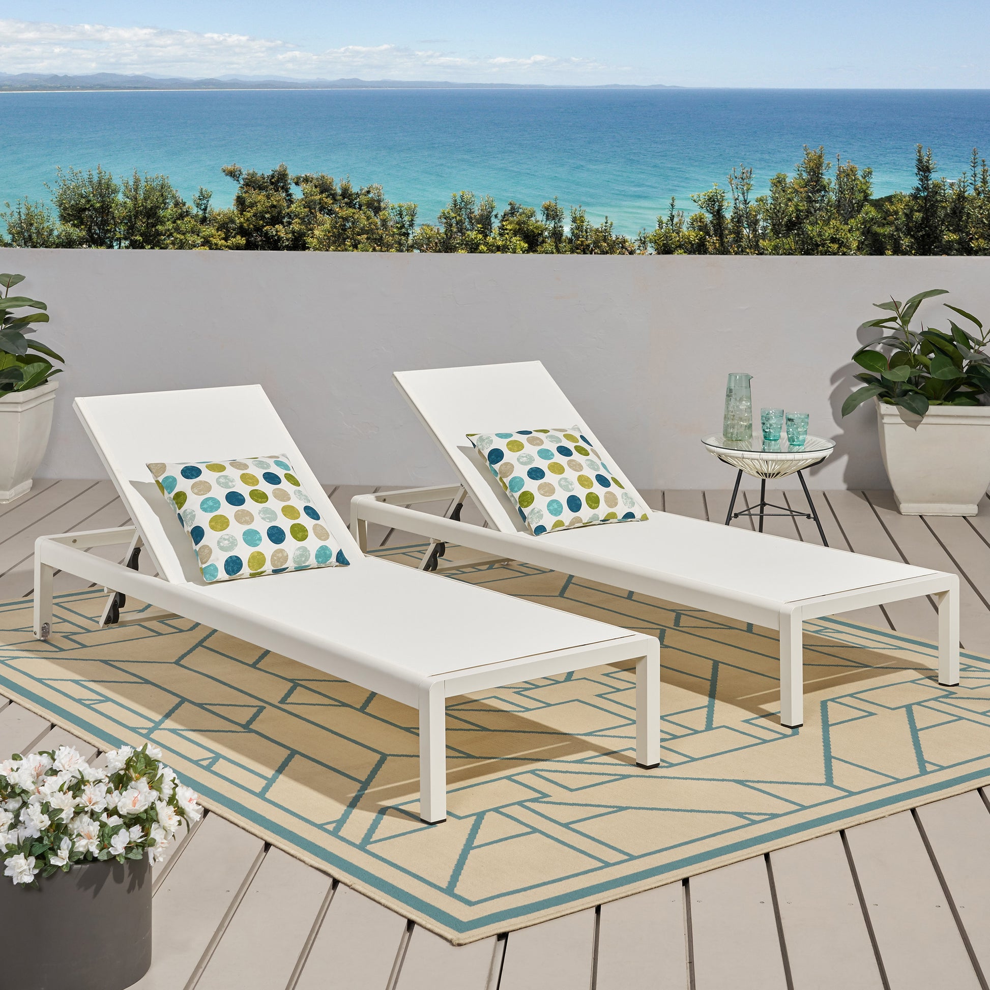 Two white aluminum chaise lounges with colorful patterned pillows on a deck overlooking the ocean