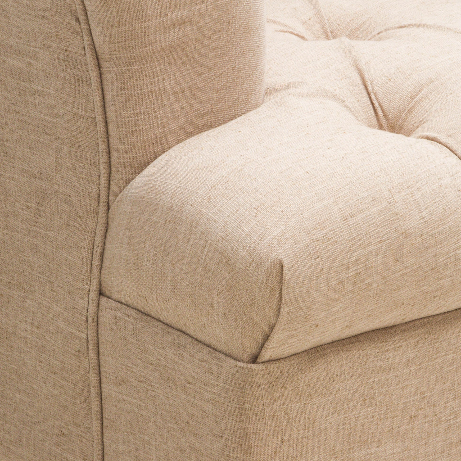 Closeup of a tufted beige linen armchair armrest with subtle texture variations