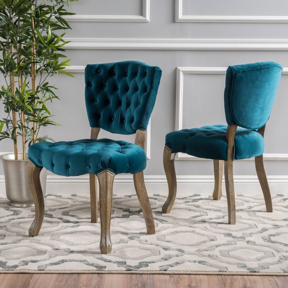 Two plush teal velvet dining chairs with tufted backs and oak legs