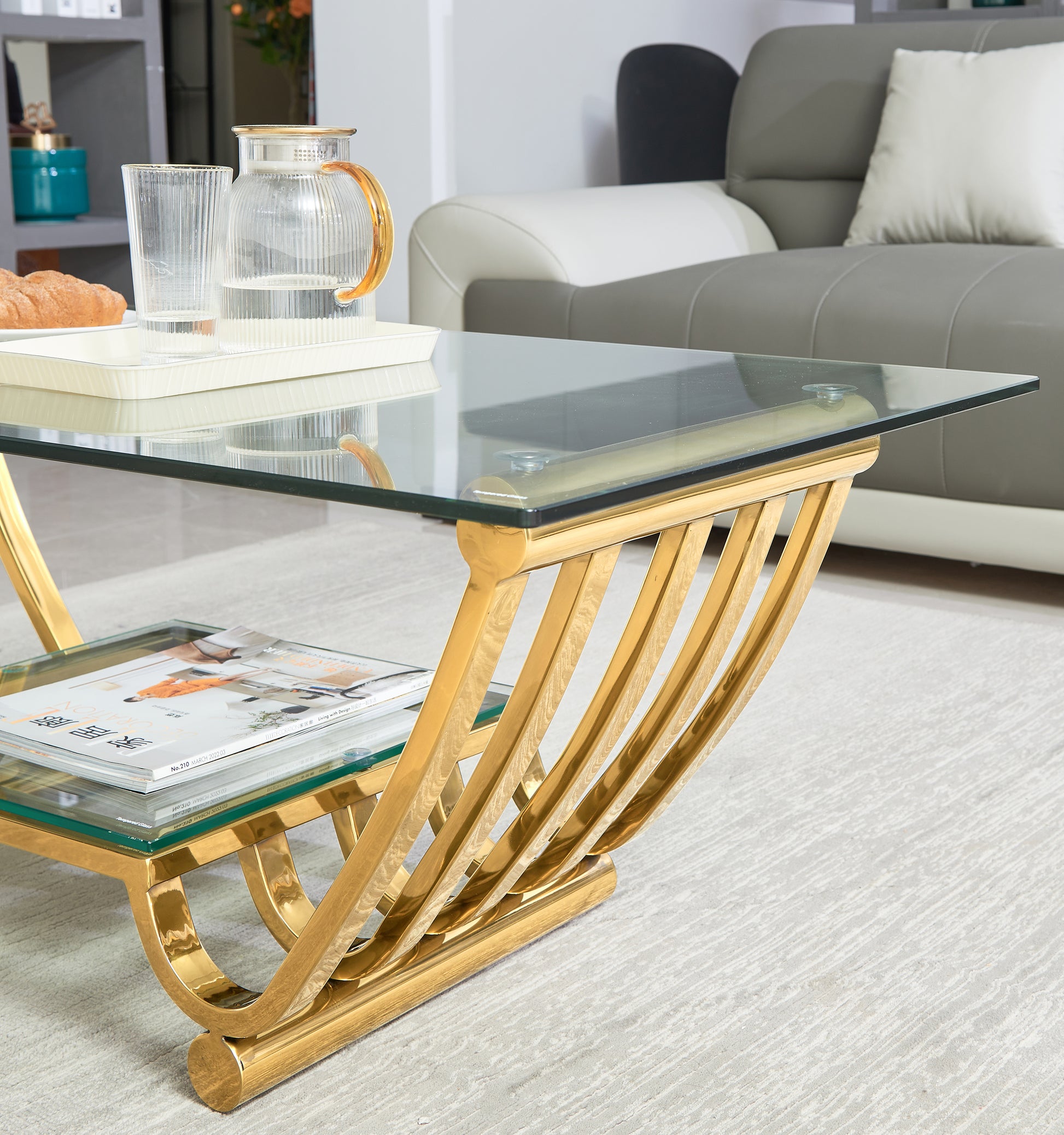 Modern gold coffee table with tempered glass top and tiered shelf featuring a sculptural base